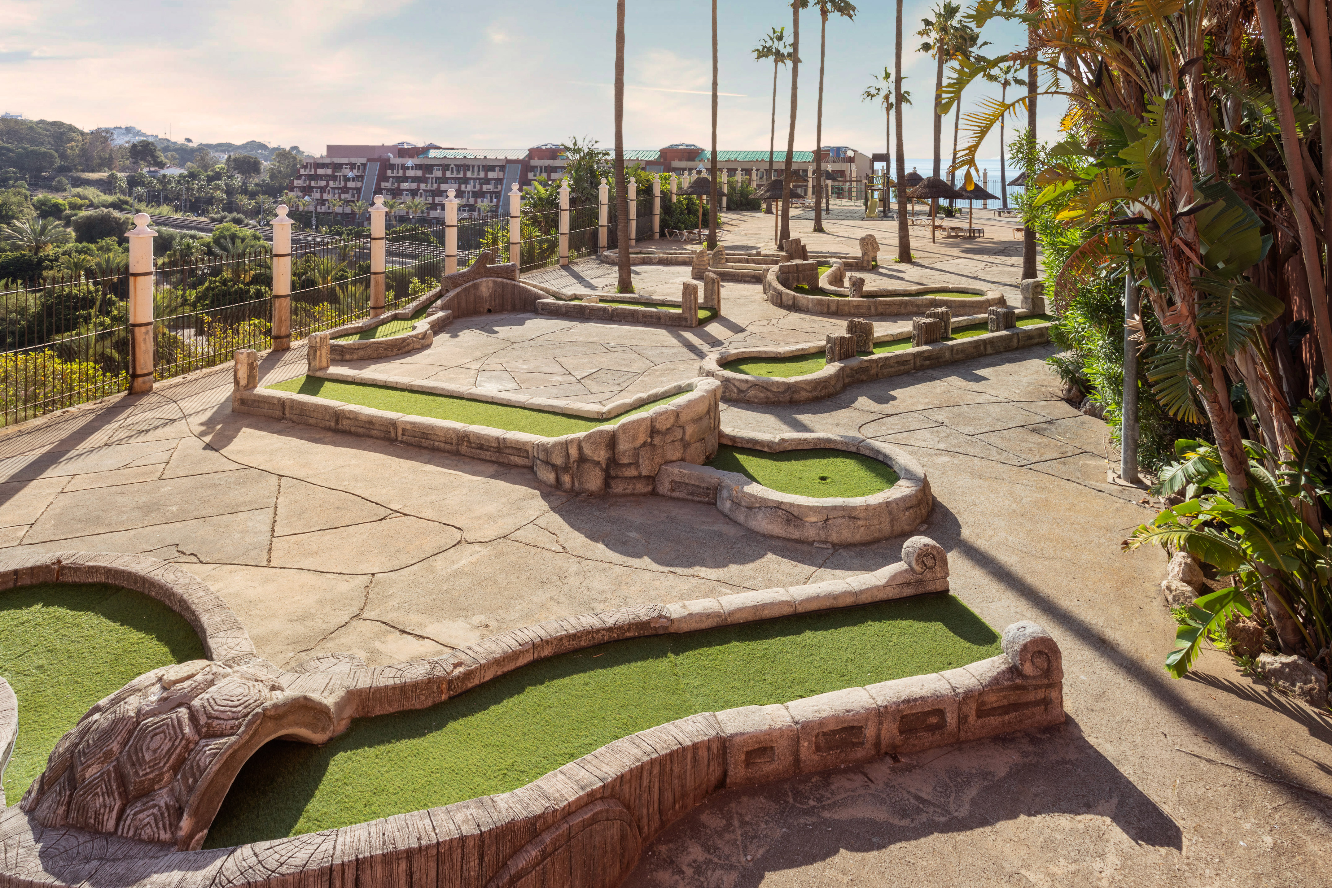 Outdoor mini-golf course with turtle obstacle, palm trees, and resort hotel.