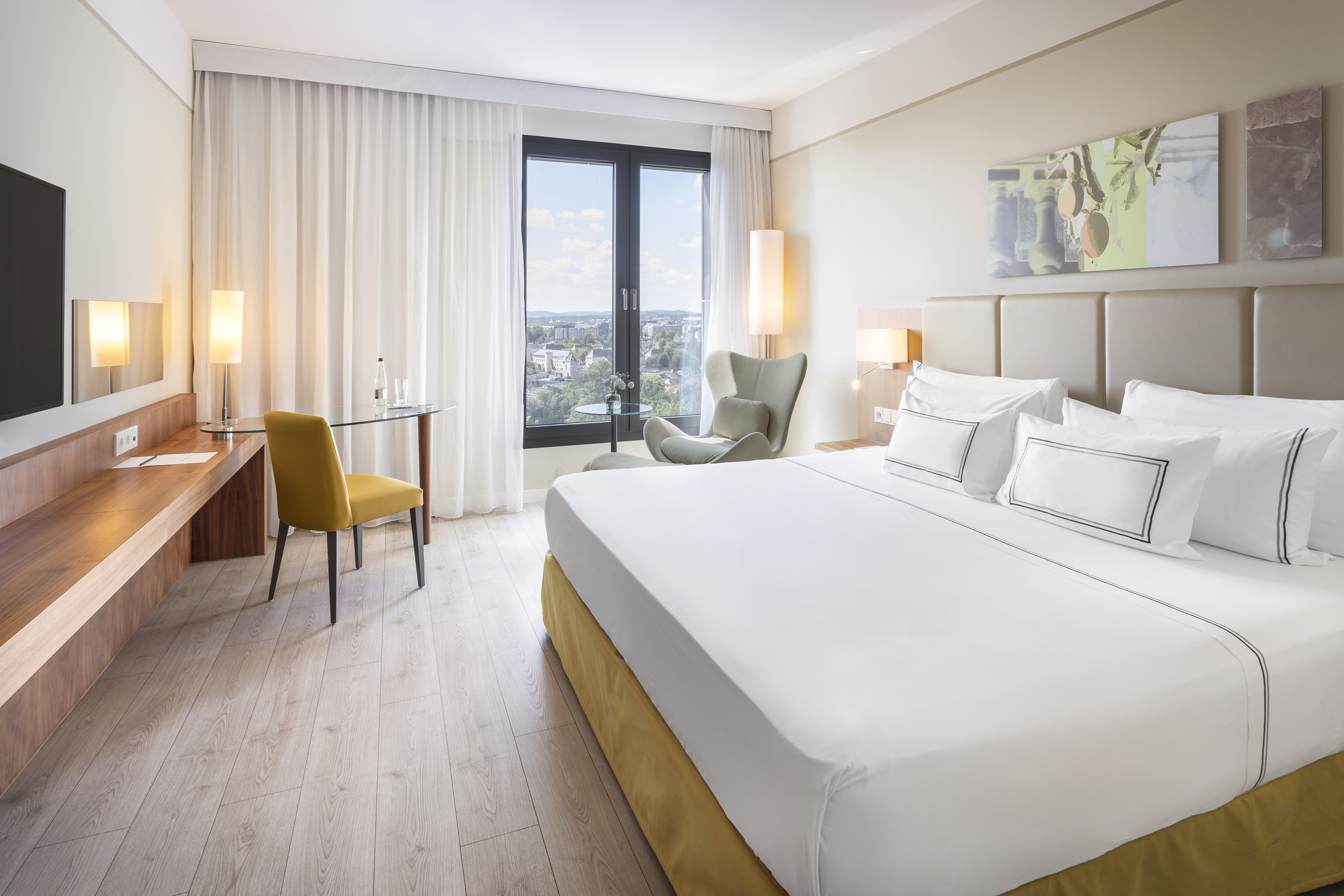Modern hotel room with large bed, city view window, and work desk.