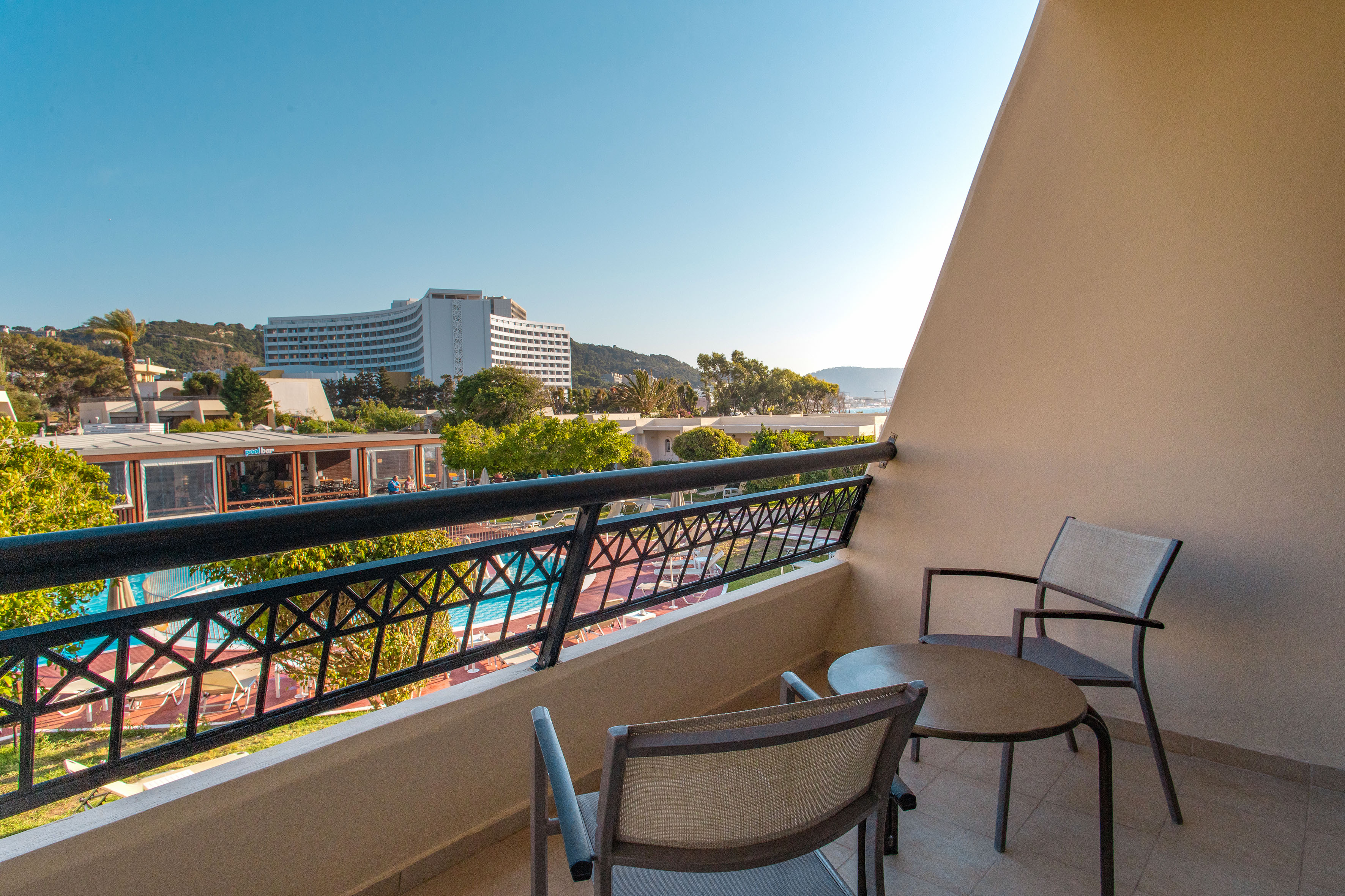 Hotel balcony with outdoor seating, overlooking resort pool and hotel building.