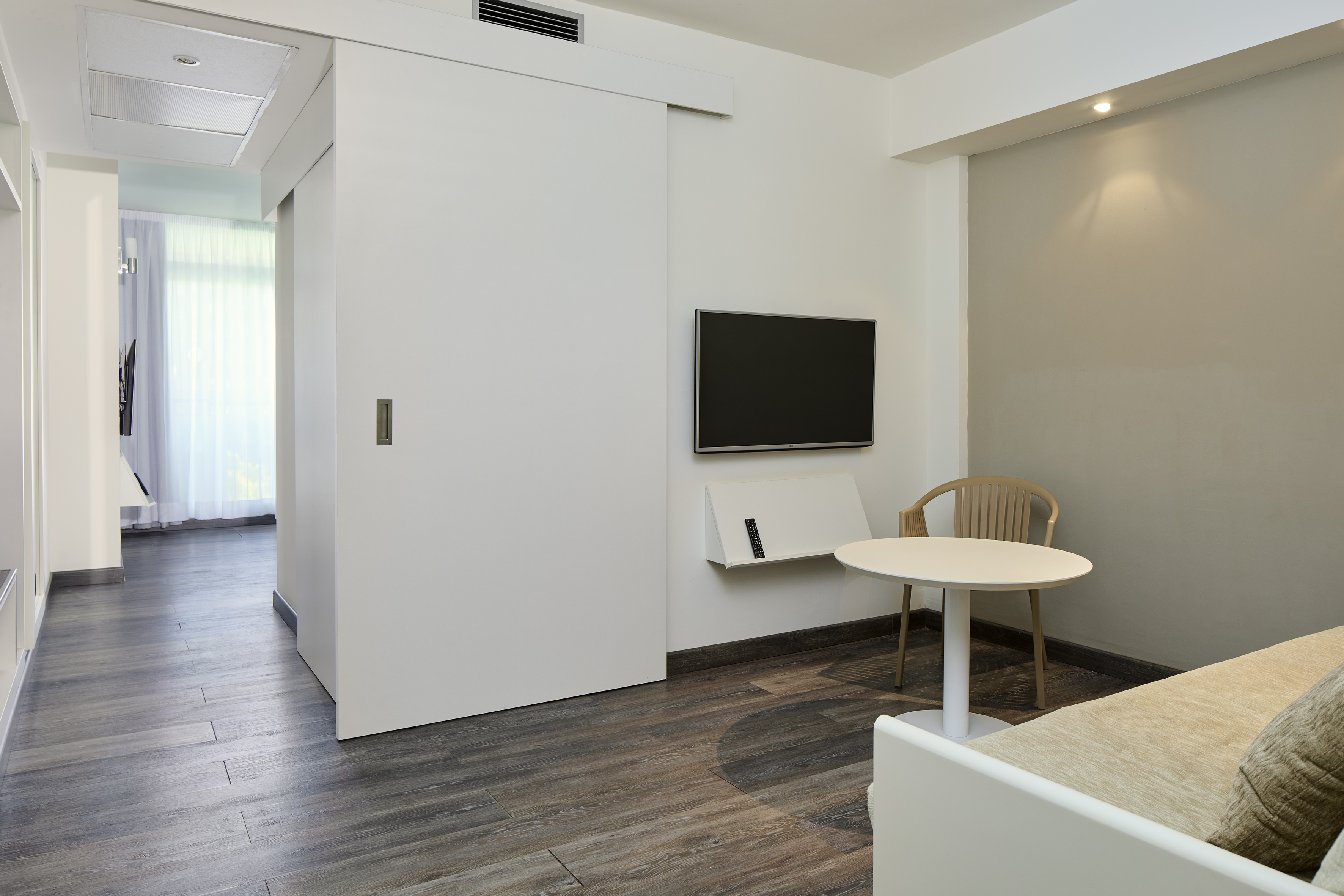 Modern studio room with sliding door, wall TV, table, chair, and wood floor.