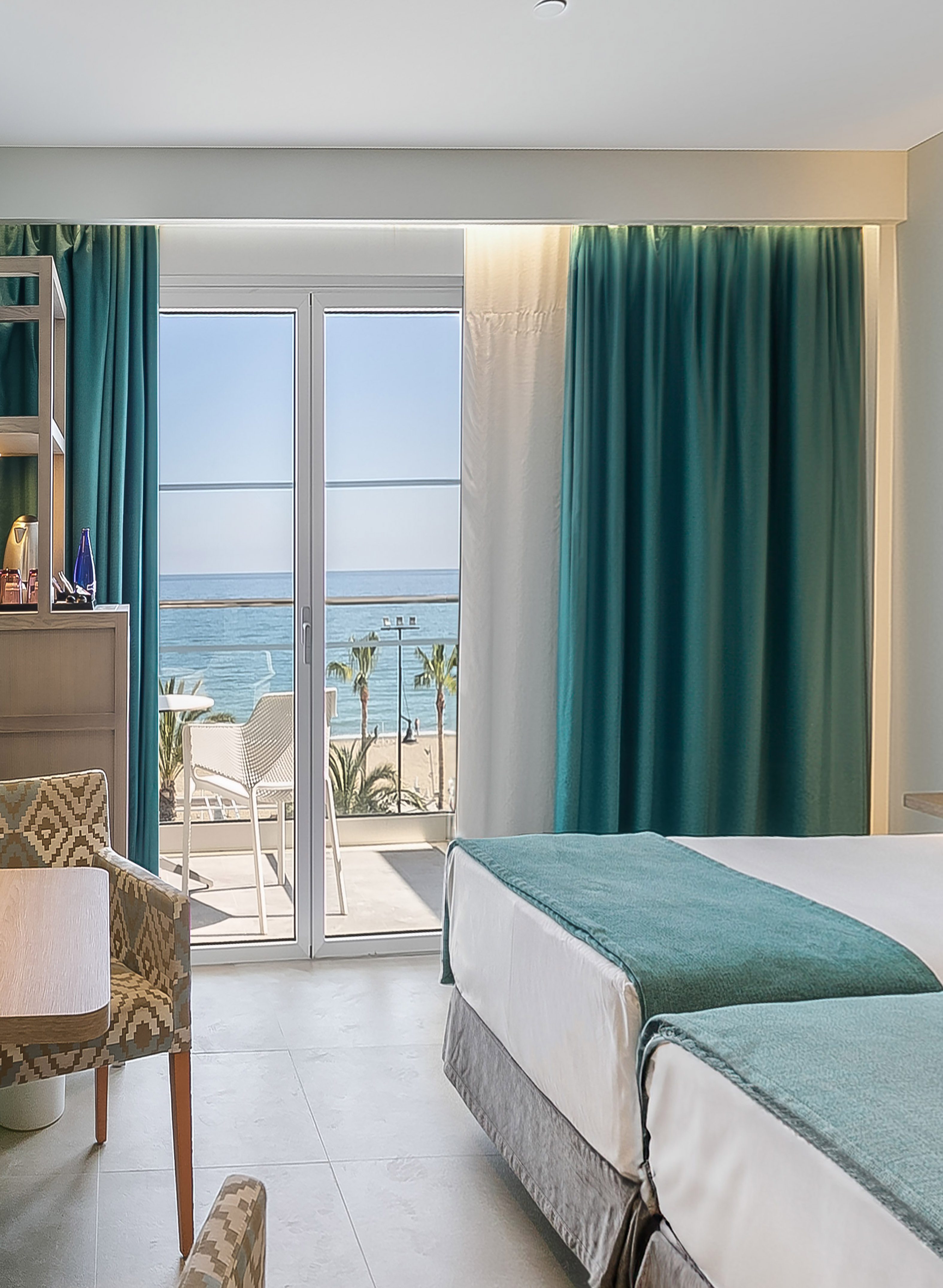 Hotel room with sea view balcony, sandy beach, and modern teal decor.