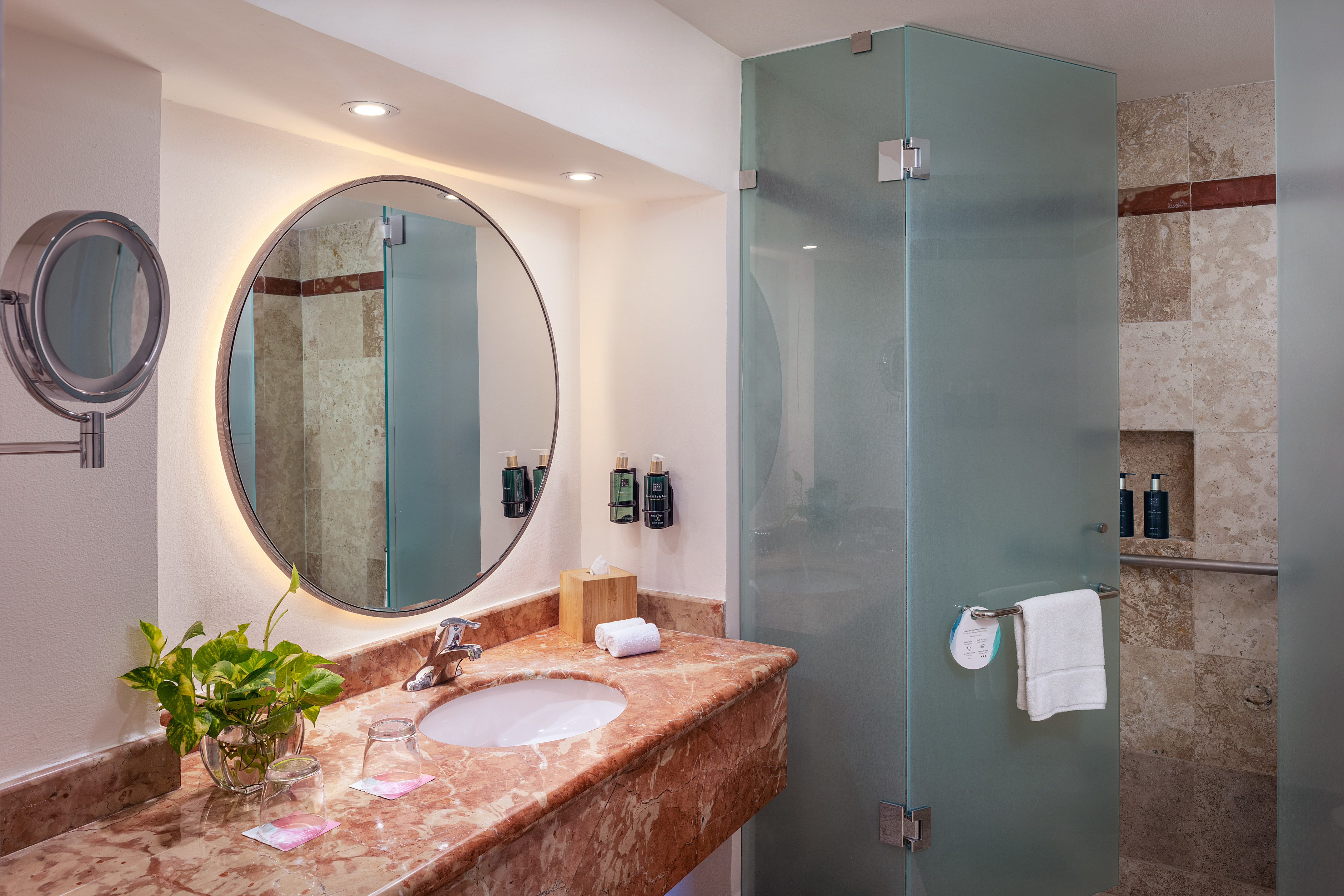 Contemporary bathroom with marble vanity, backlit mirror, and glass shower.