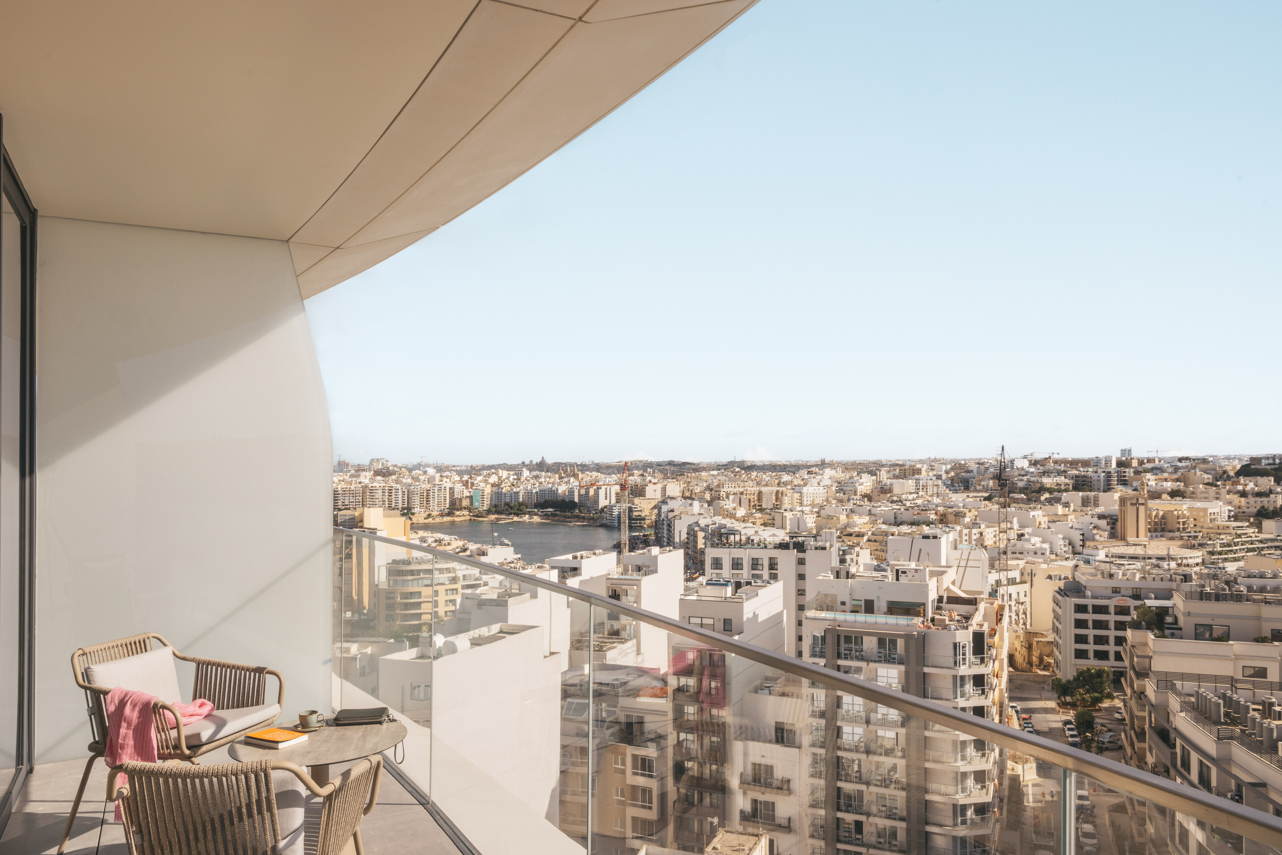 Modern balcony with outdoor chairs, city skyline, and distant harbor view.