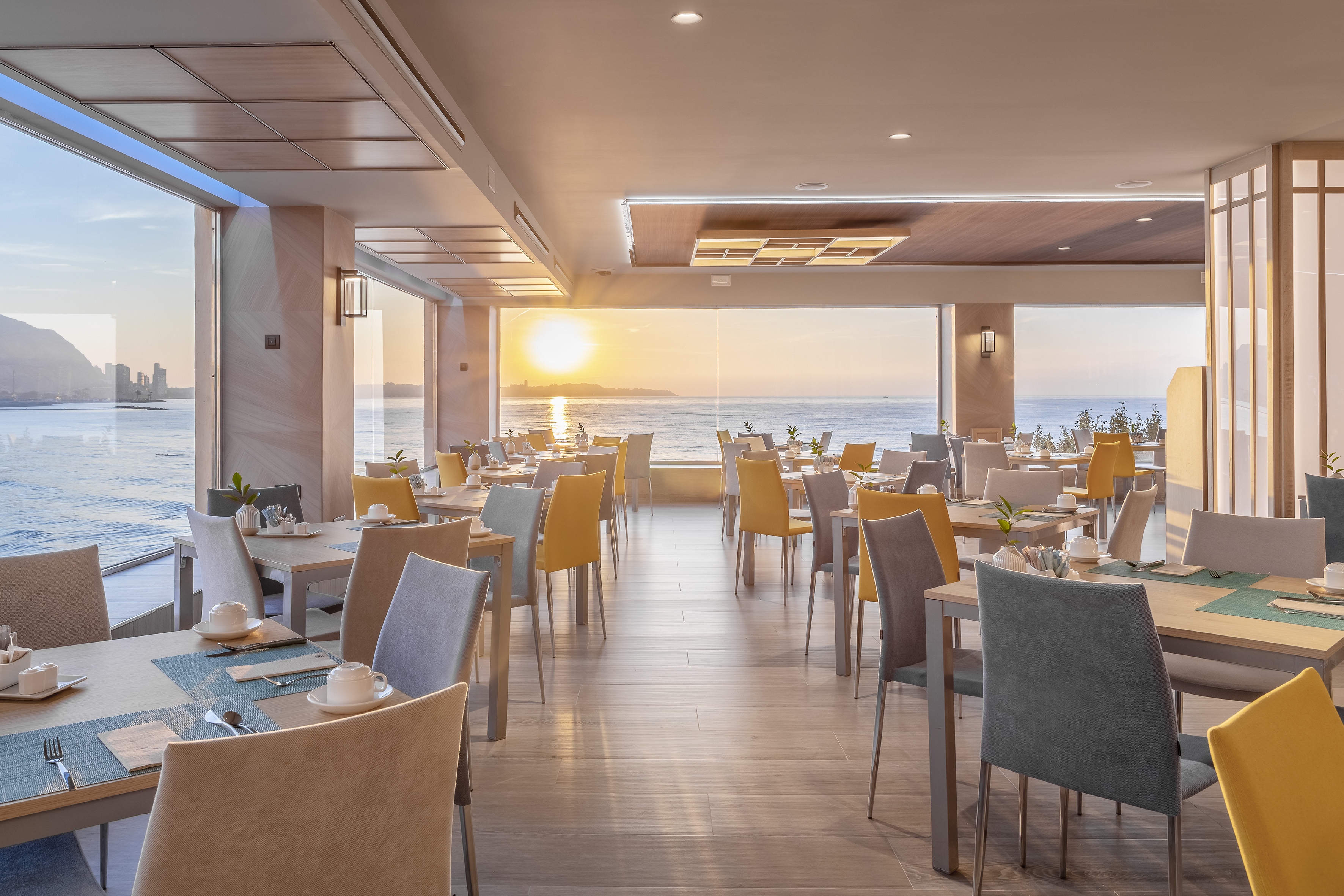 Modern oceanfront restaurant with sunset view, tables set for dining.