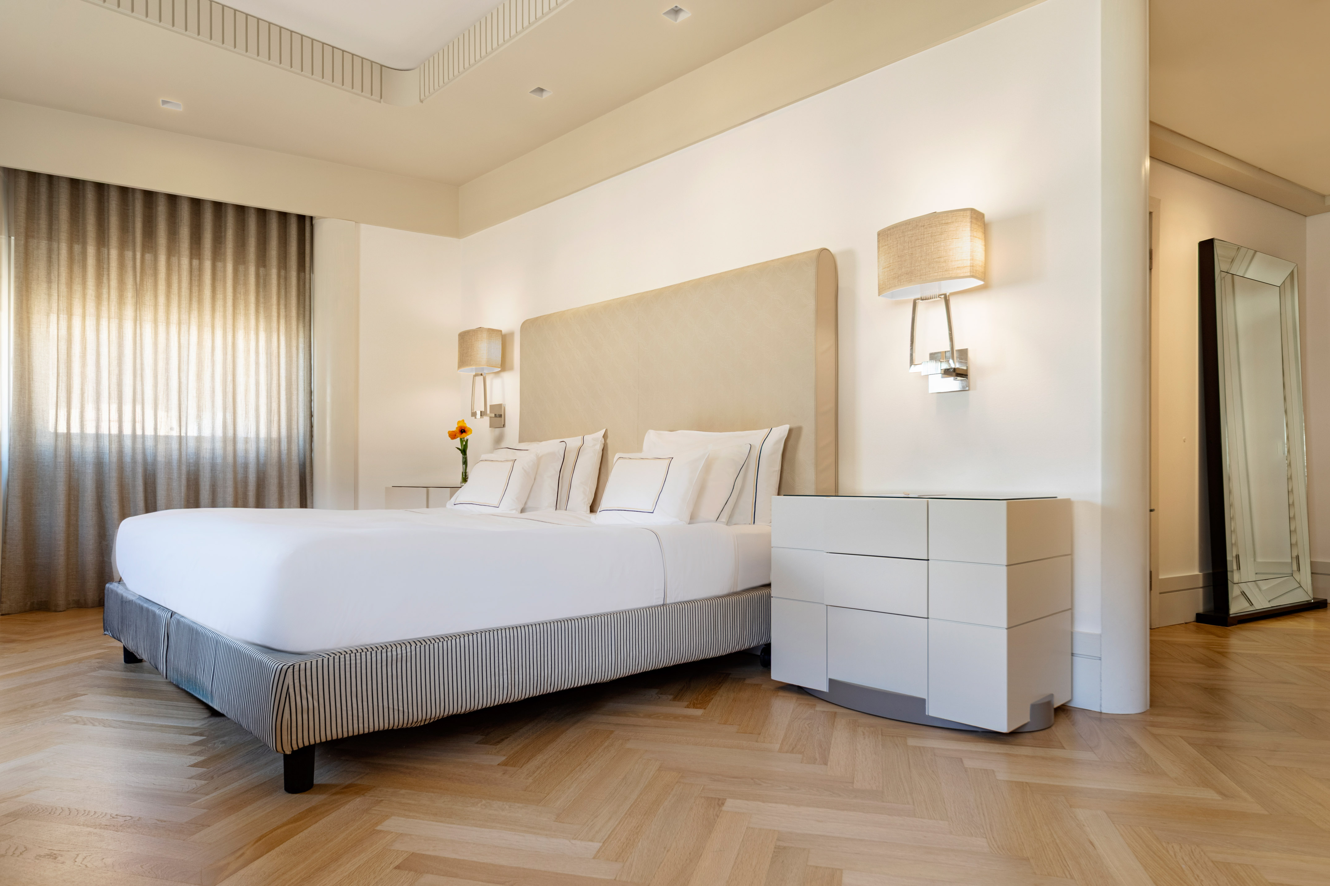 Elegant bedroom with king bed, neutral decor, and herringbone wood floor.