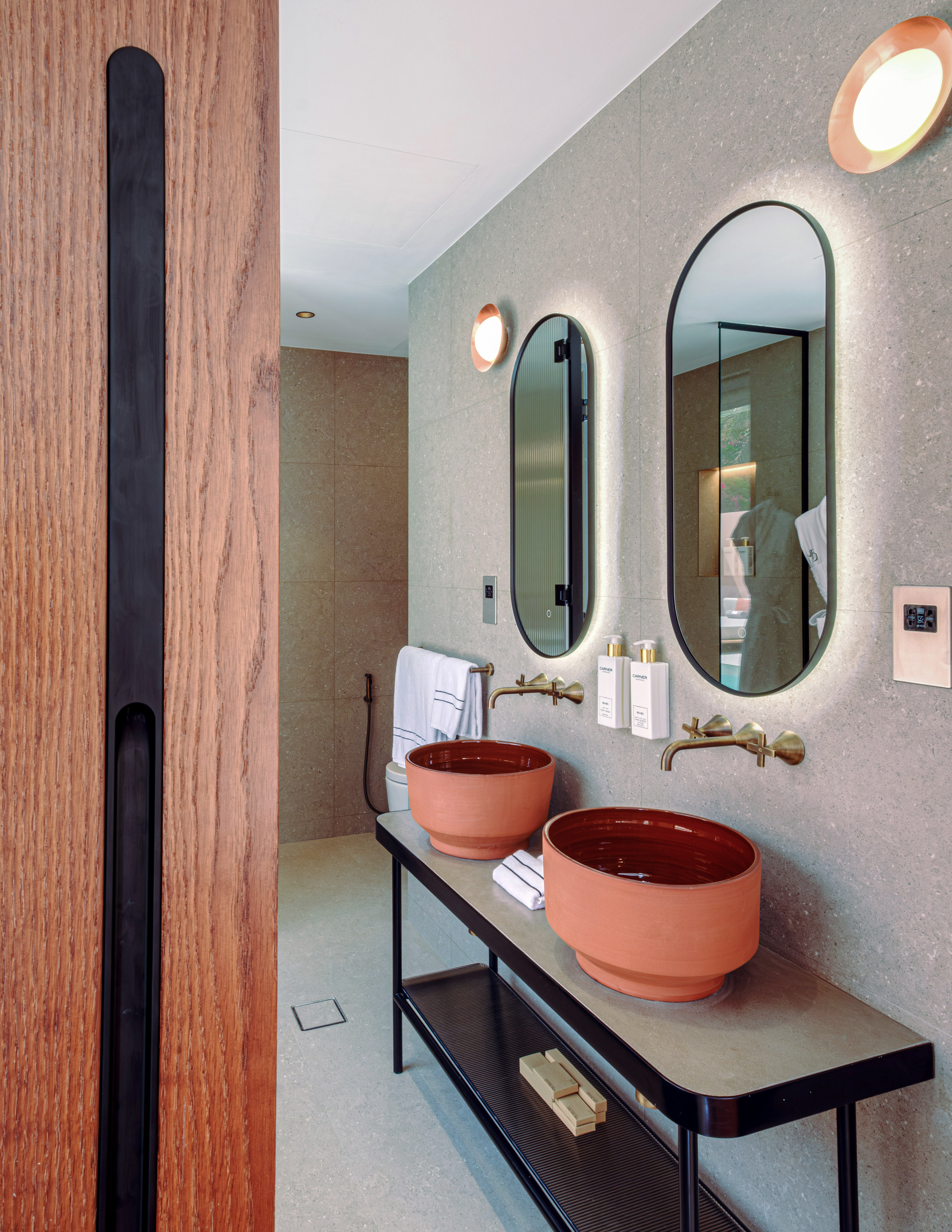 Modern bathroom with twin terracotta basins, gold faucets, and backlit mirrors.