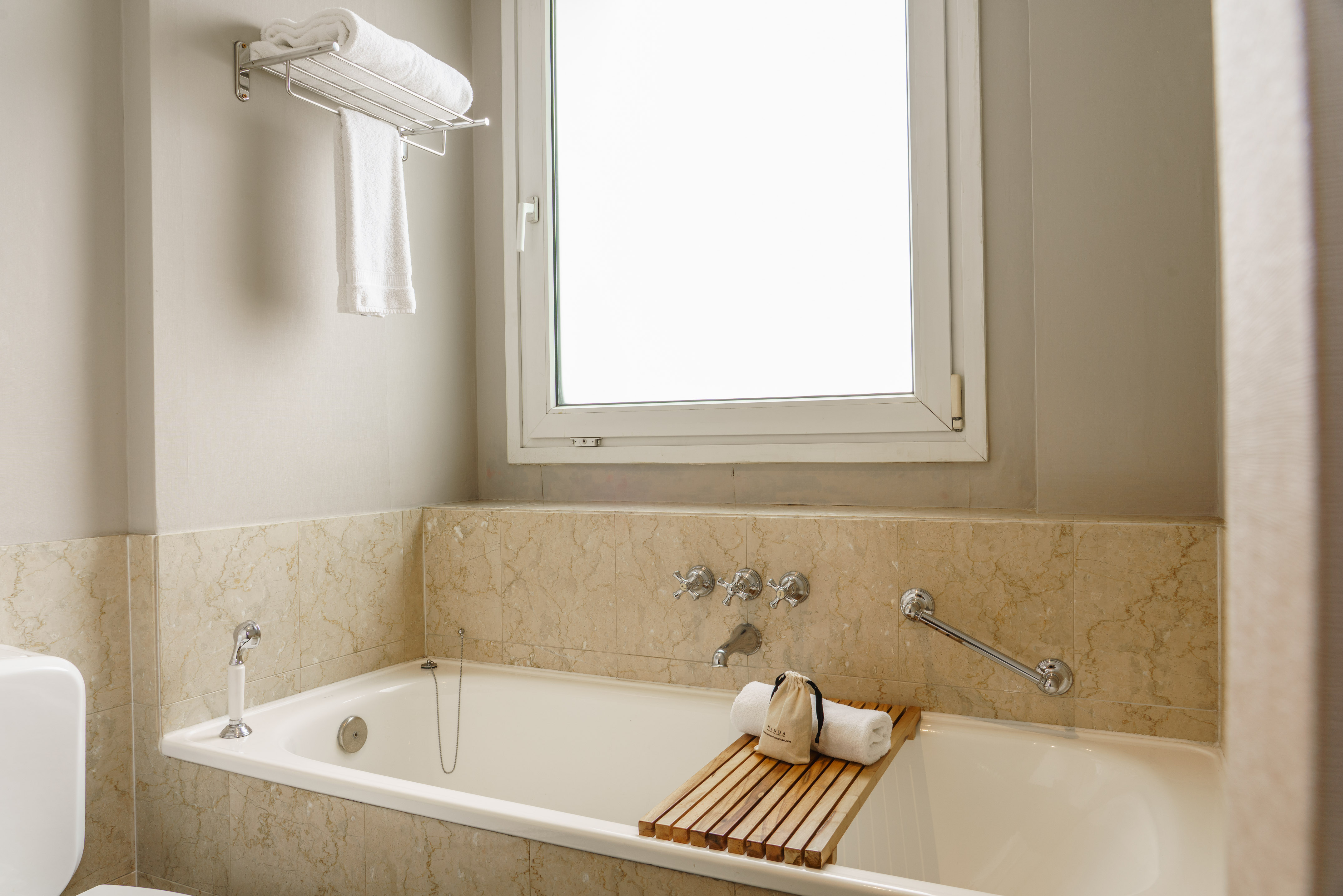 White bathtub and marble bathroom with window, towels, and bath caddy.