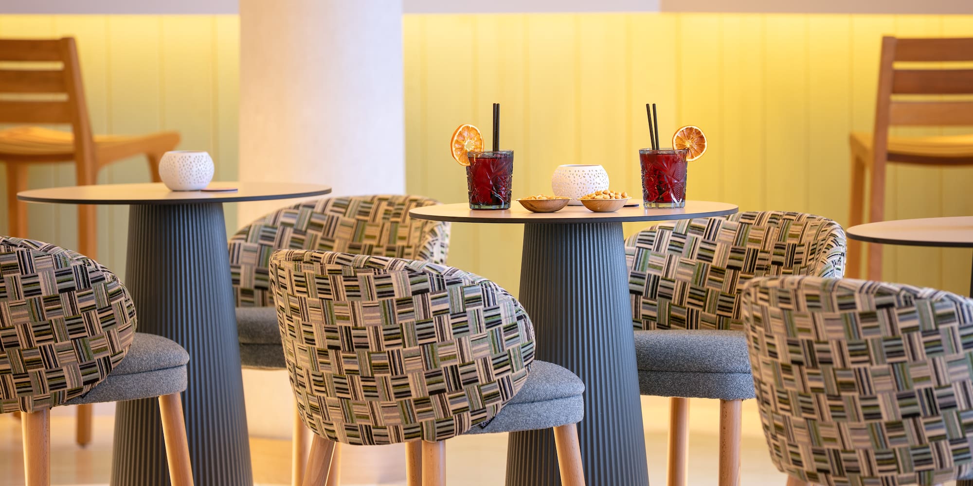 Modern bar interior with red cocktails, patterned high chairs, and yellow lighting.