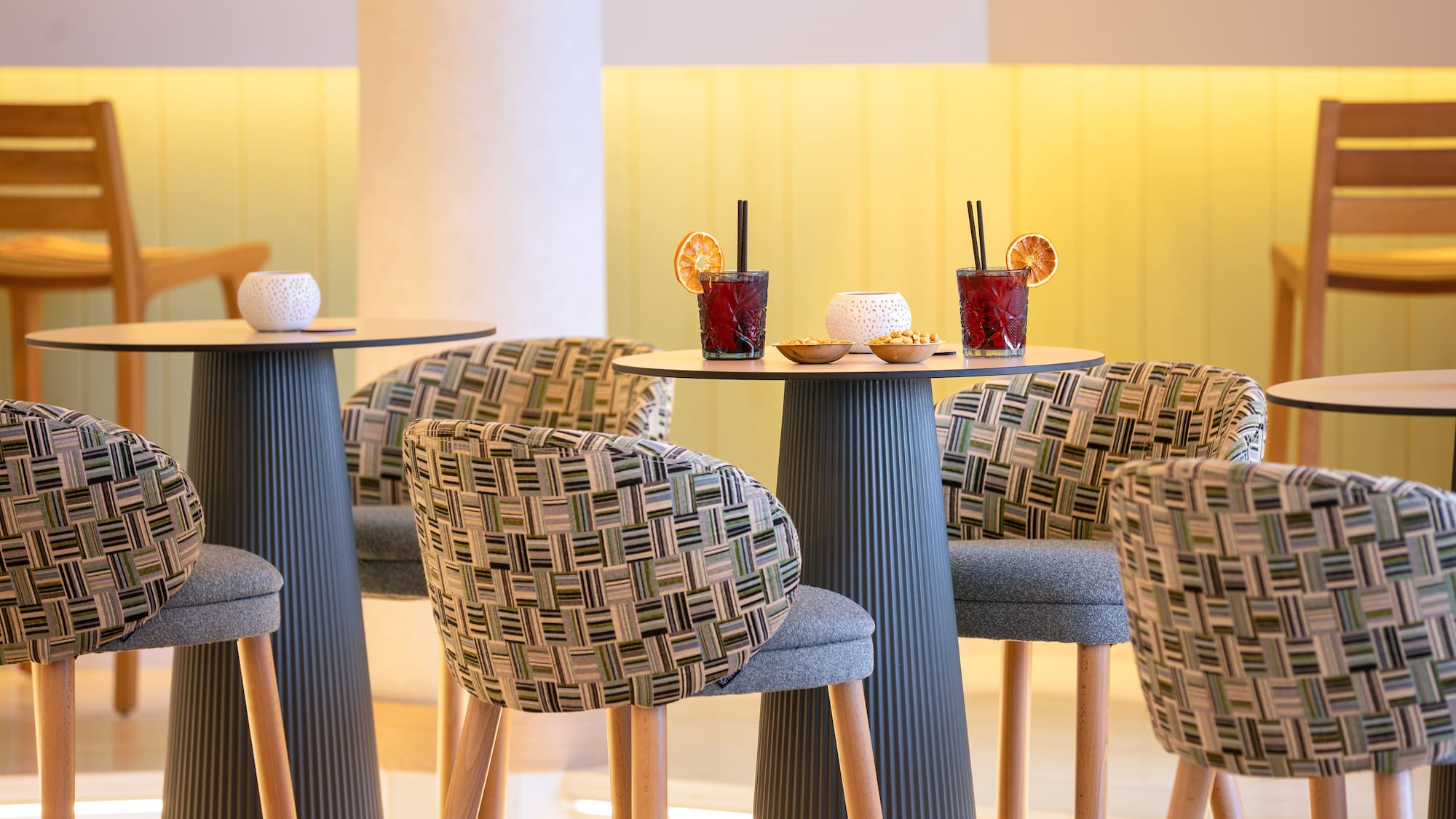 Modern bar interior with red cocktails, patterned high chairs, and yellow lighting.
