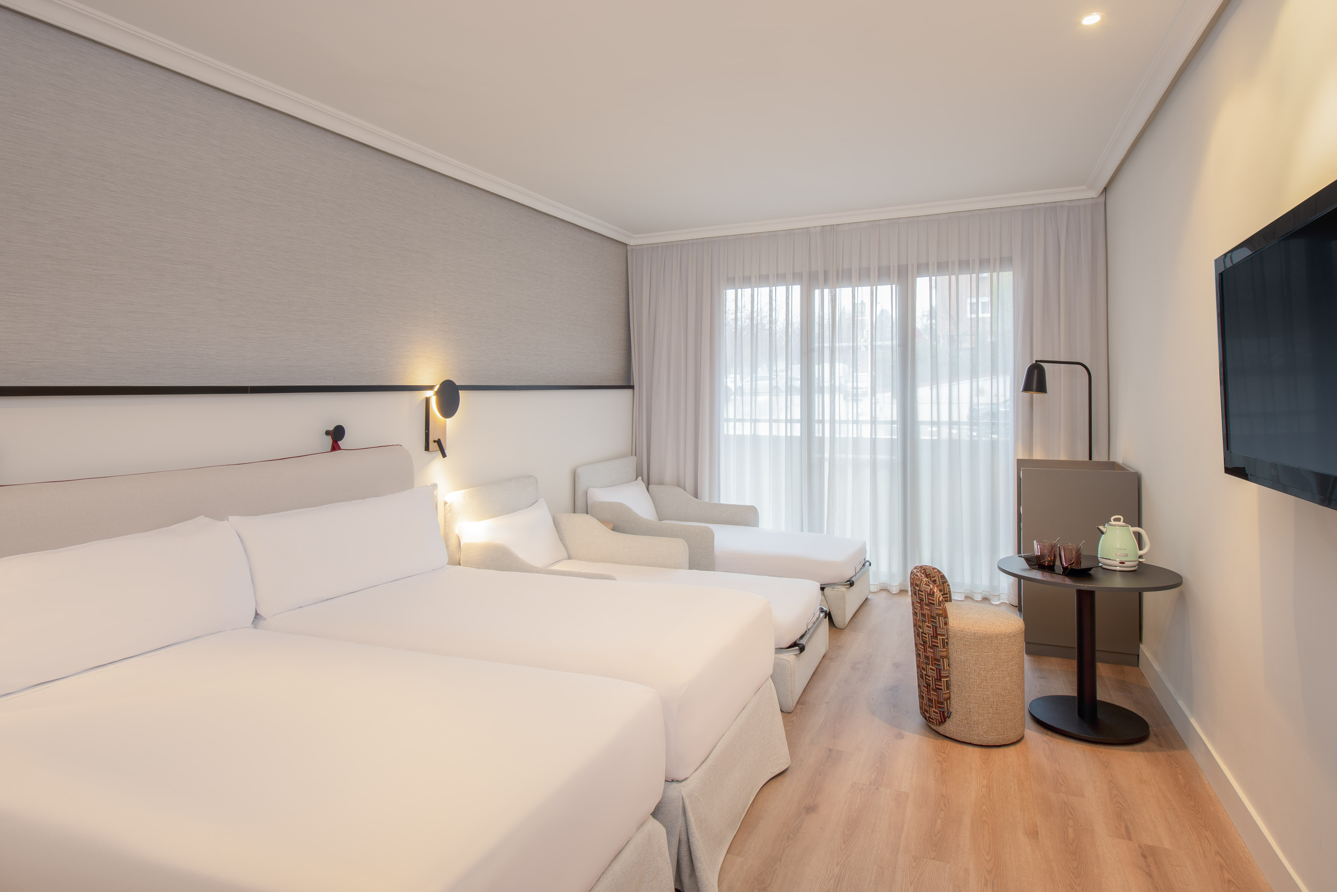 Modern hotel room, twin beds, two convertible chaises, TV, and window.