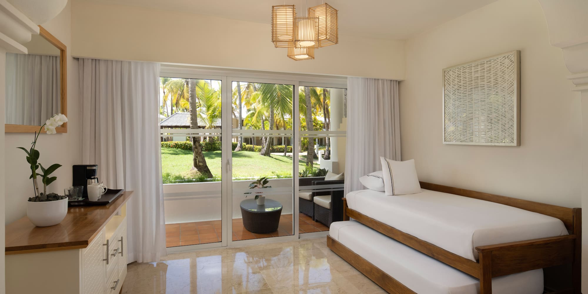 Tropical resort room with trundle bed and palm garden patio view.