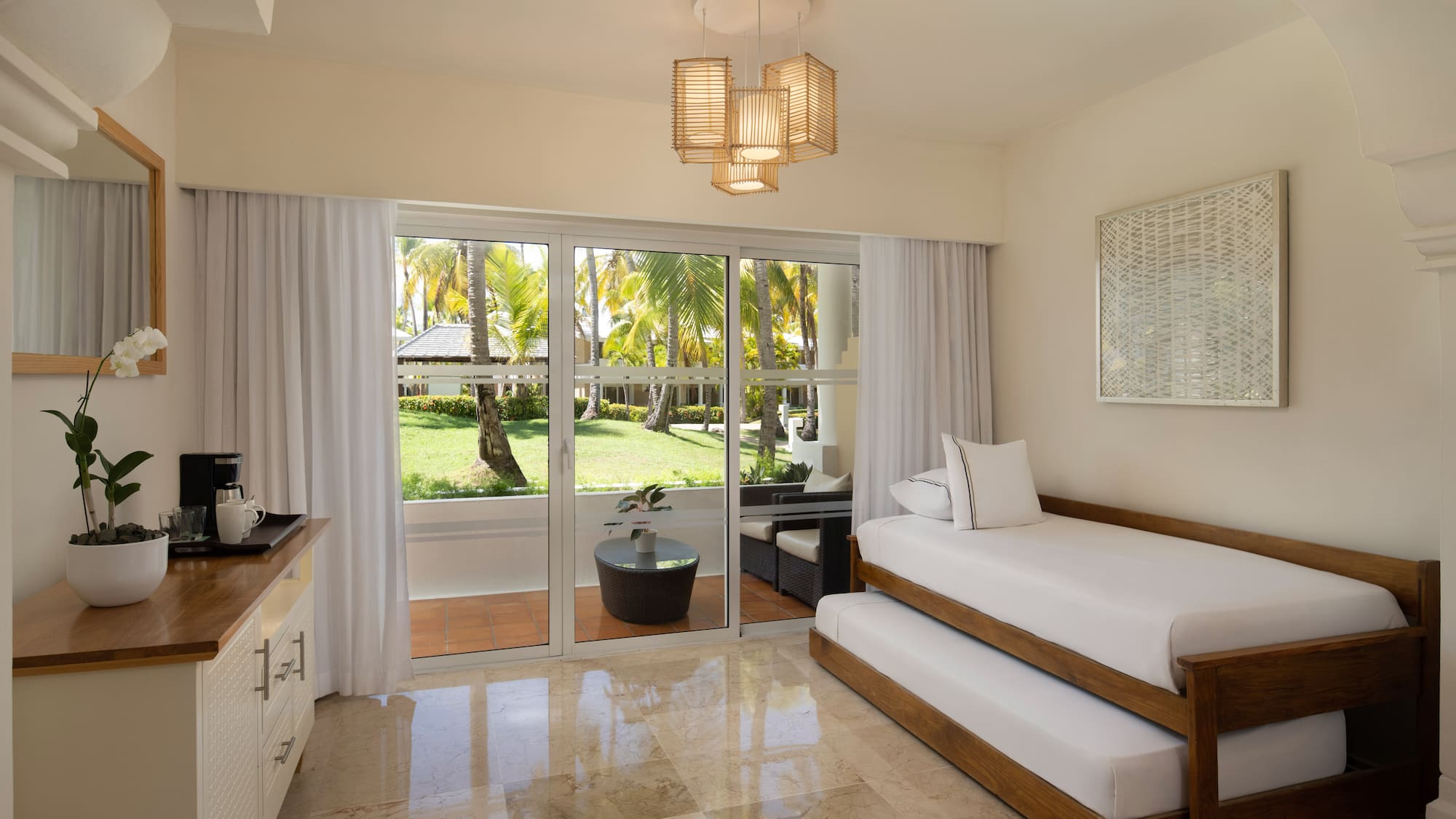 Tropical resort room with trundle bed and palm garden patio view.