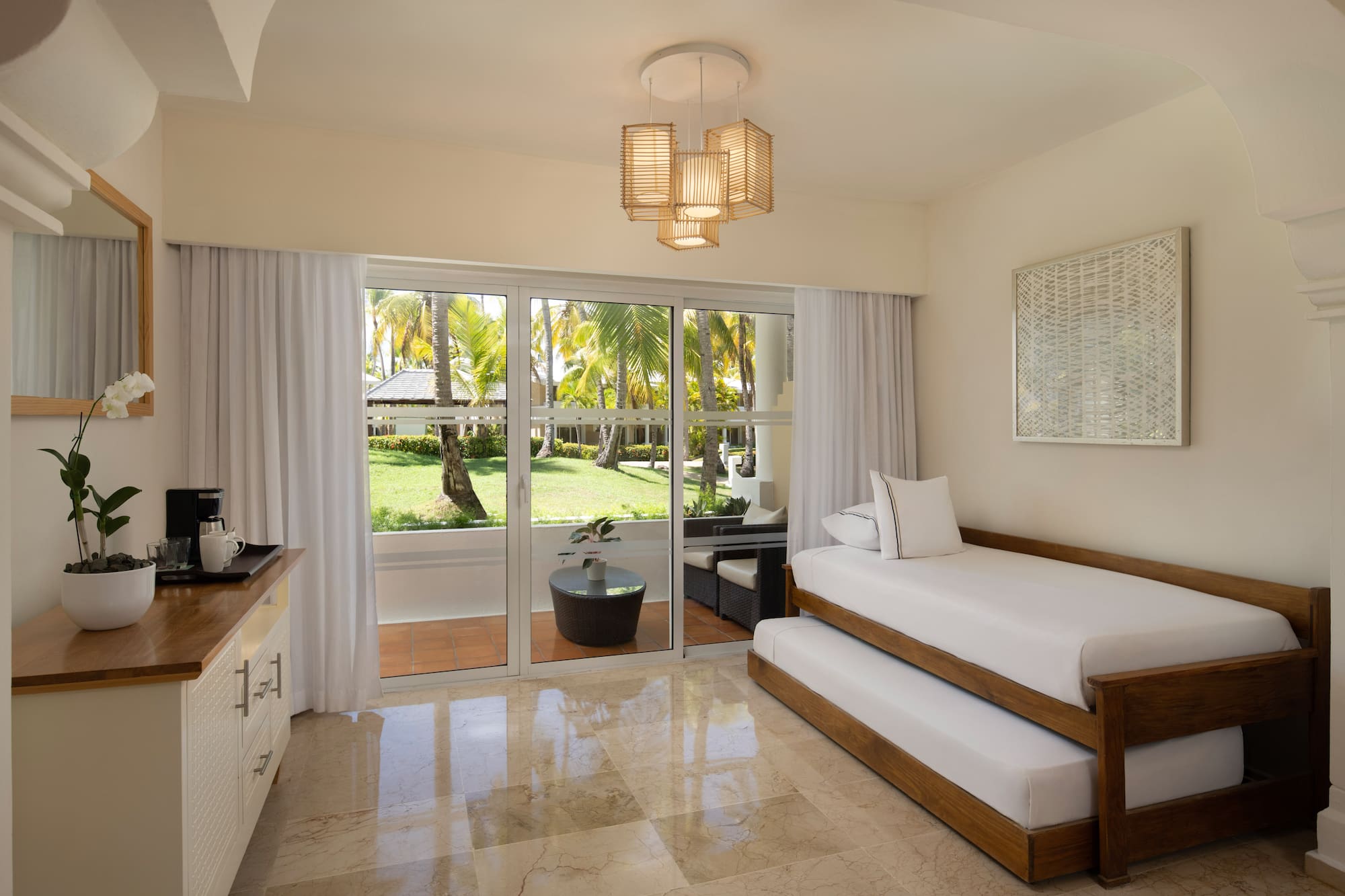 Tropical resort room with trundle bed and palm garden patio view.
