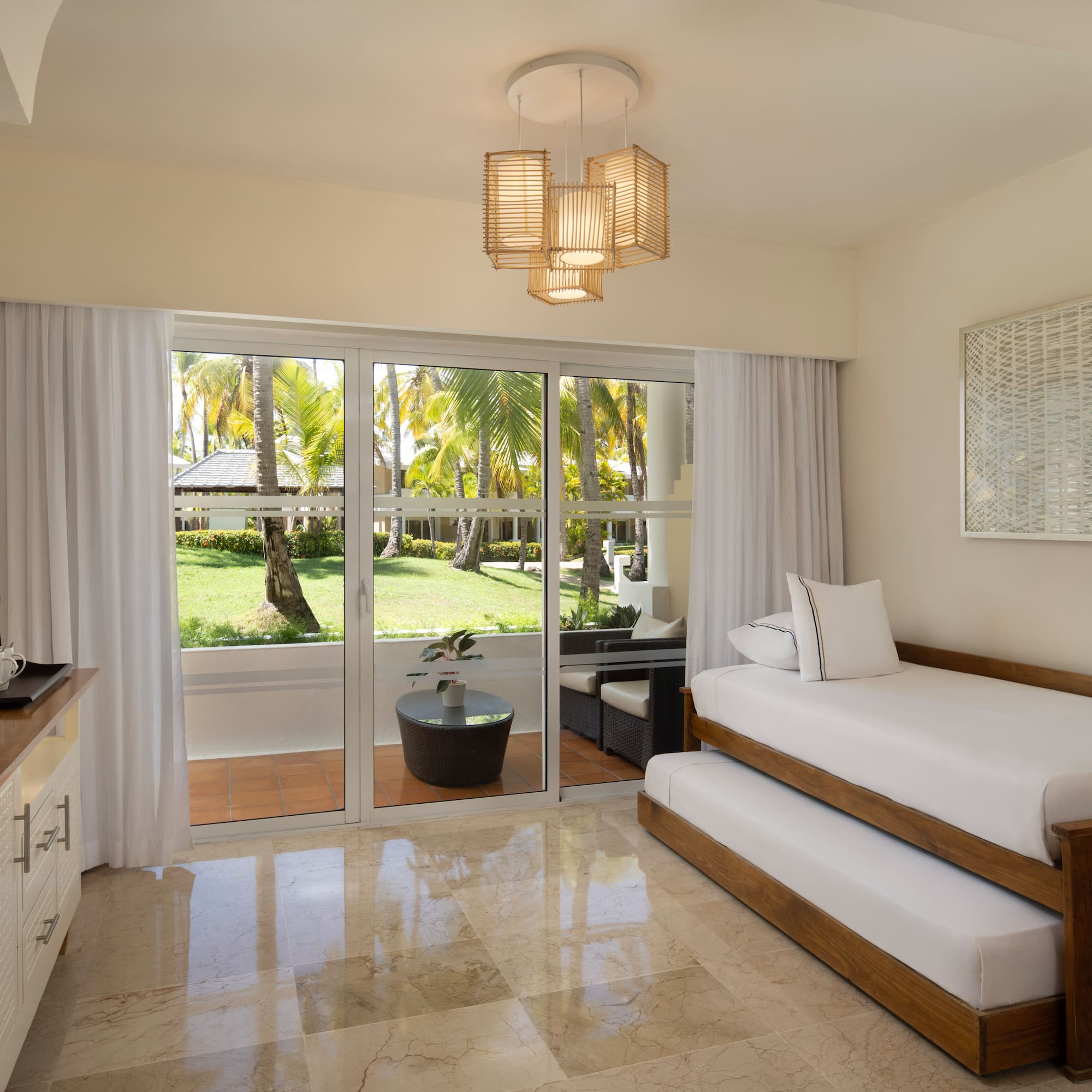 Tropical resort room with trundle bed and palm garden patio view.