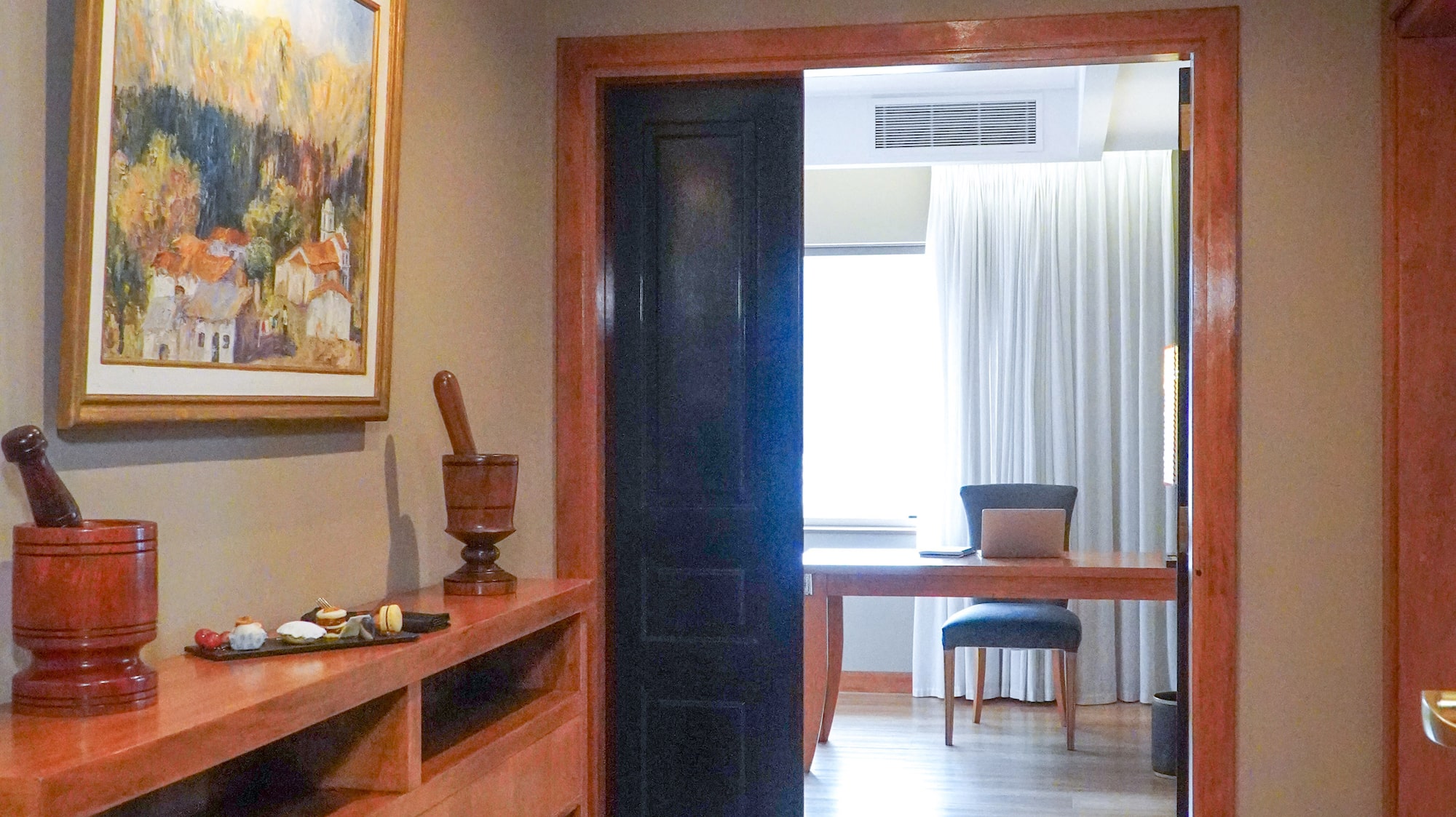 Hotel suite hallway with wooden console, landscape painting, and bright room.