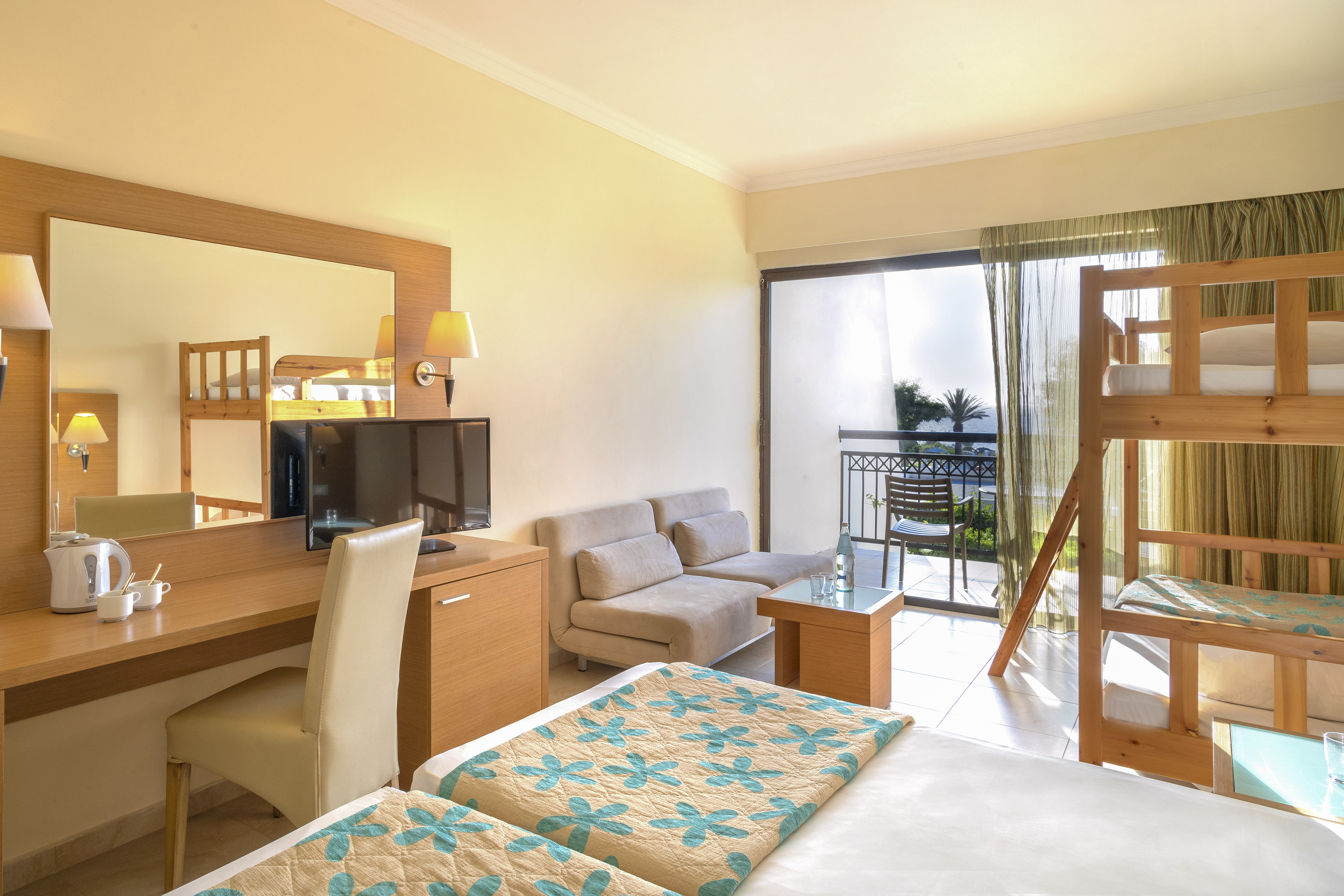 Hotel family room with bunk beds, desk, TV, and balcony sea view.
