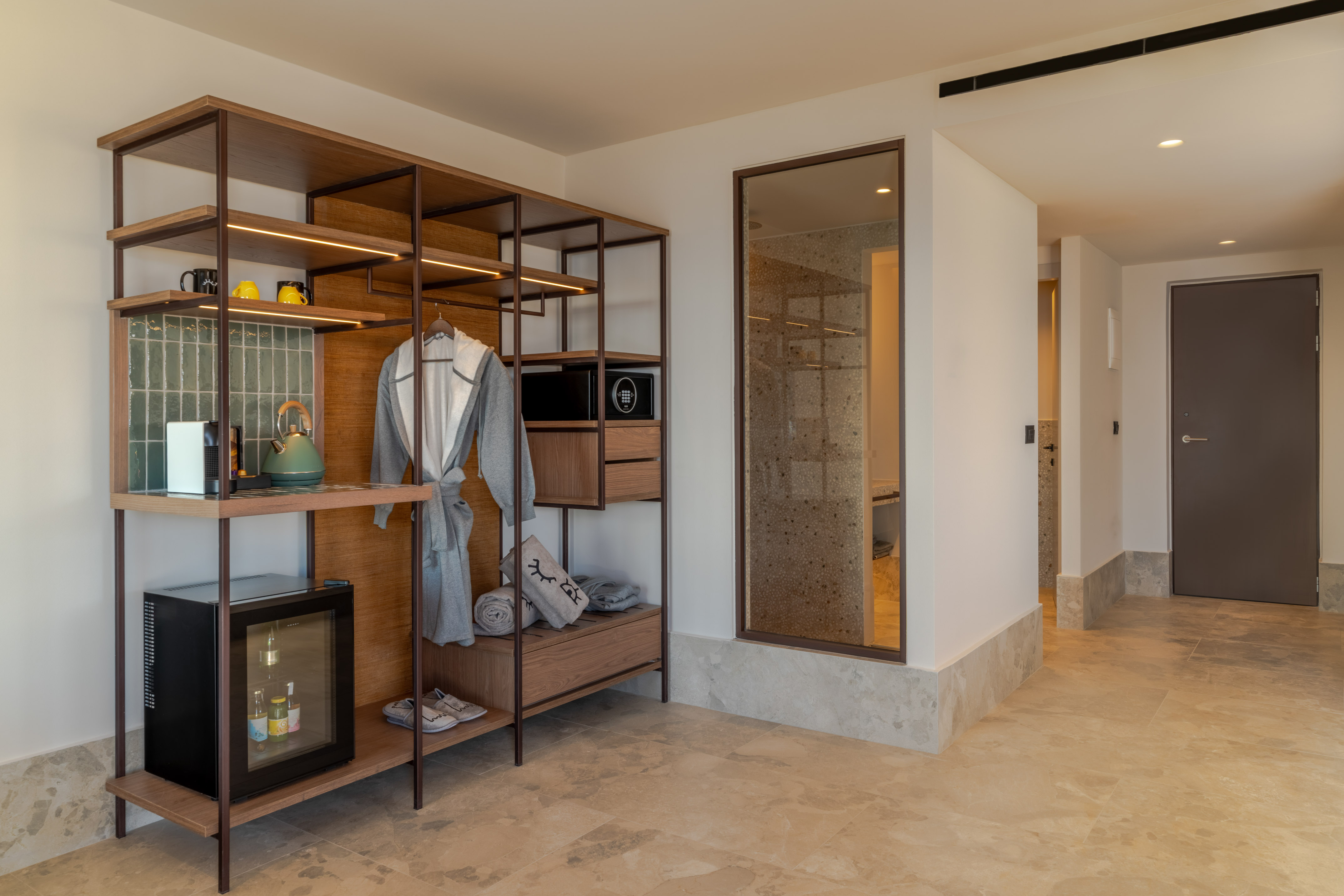 Modern hotel room closet with mini-bar, coffee station, and bathrobe.