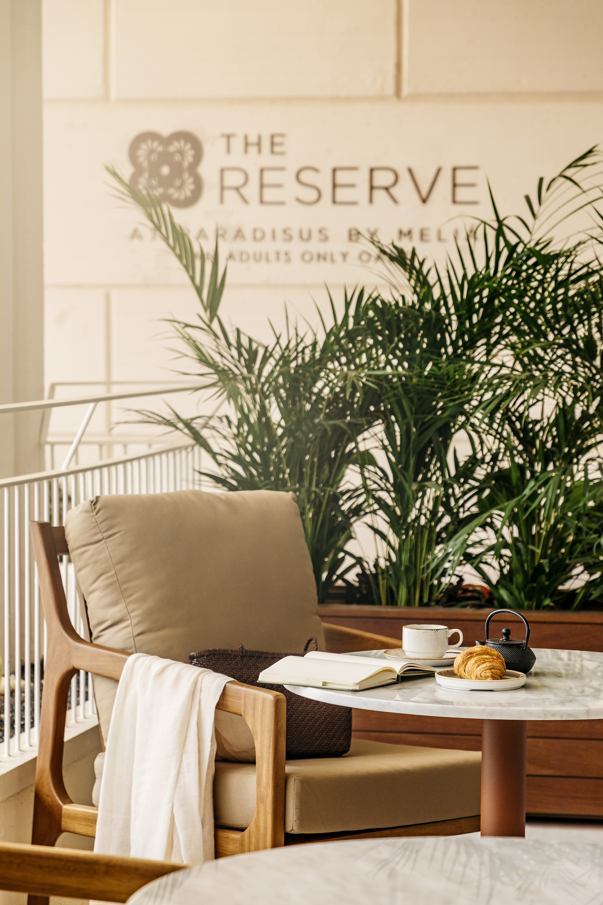 Outdoor hotel lounge at The Reserve with coffee, croissant, notebook, and plants.