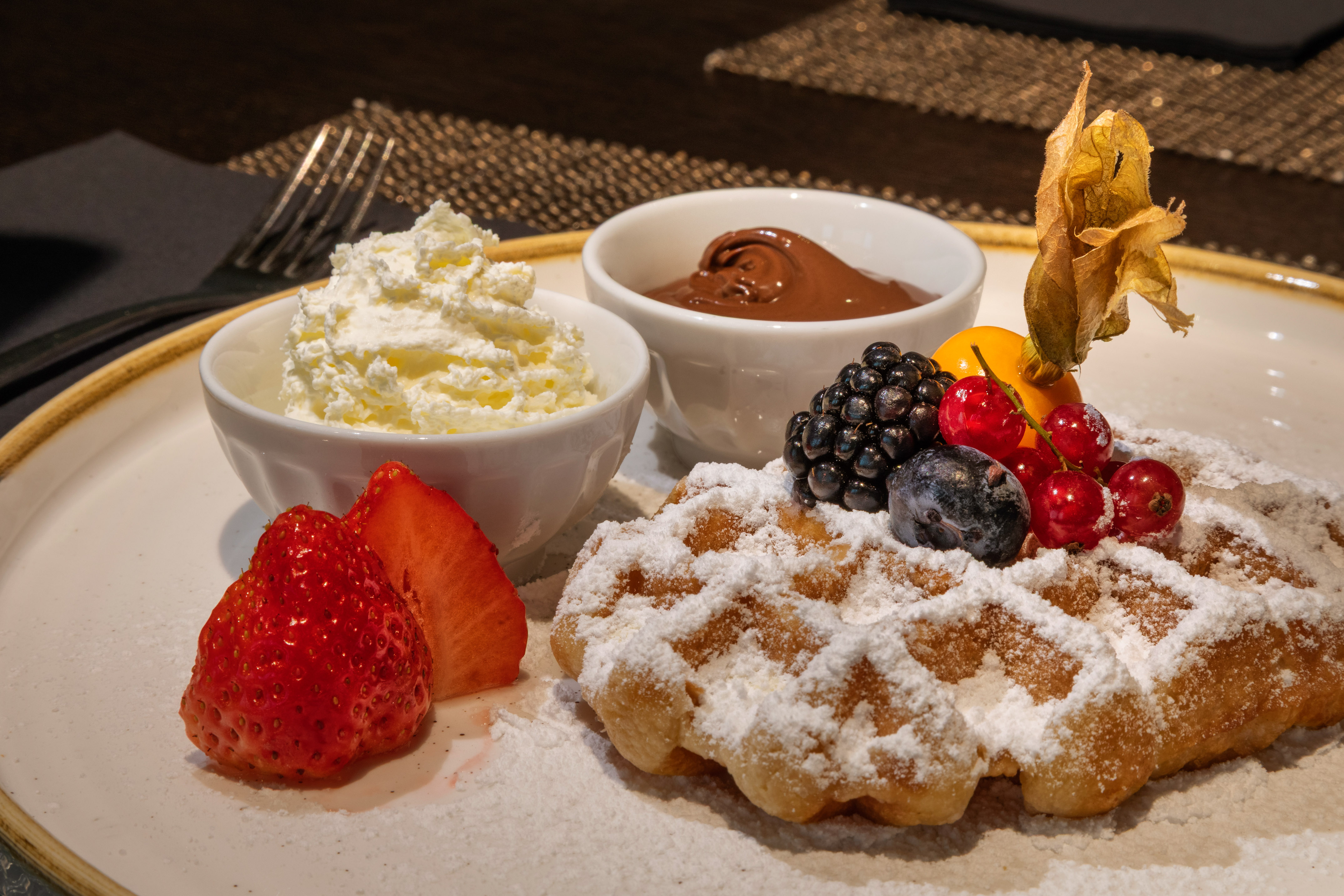 Berry waffle with powdered sugar, strawberries, whipped cream, and chocolate.