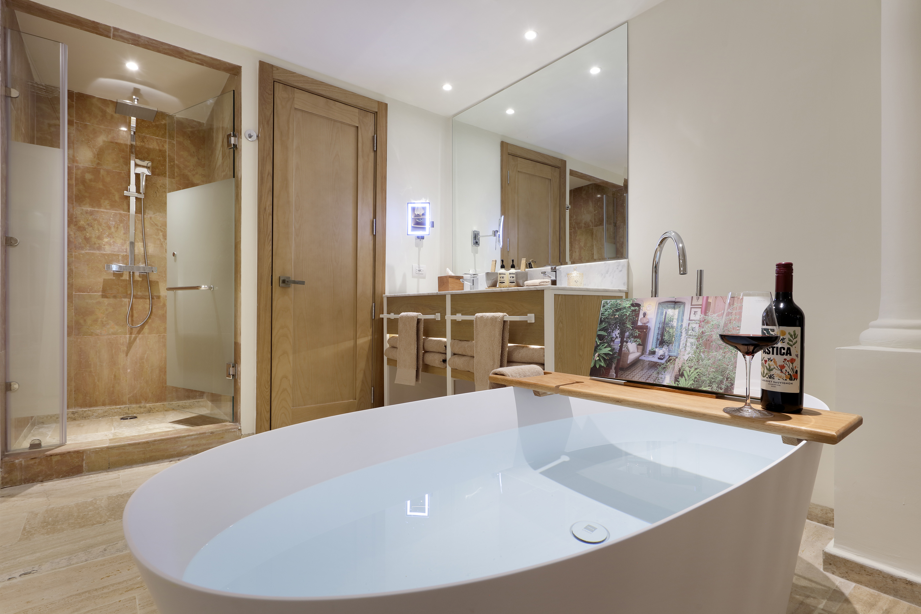 Modern bathroom with freestanding tub, walk-in shower, wine, and book.