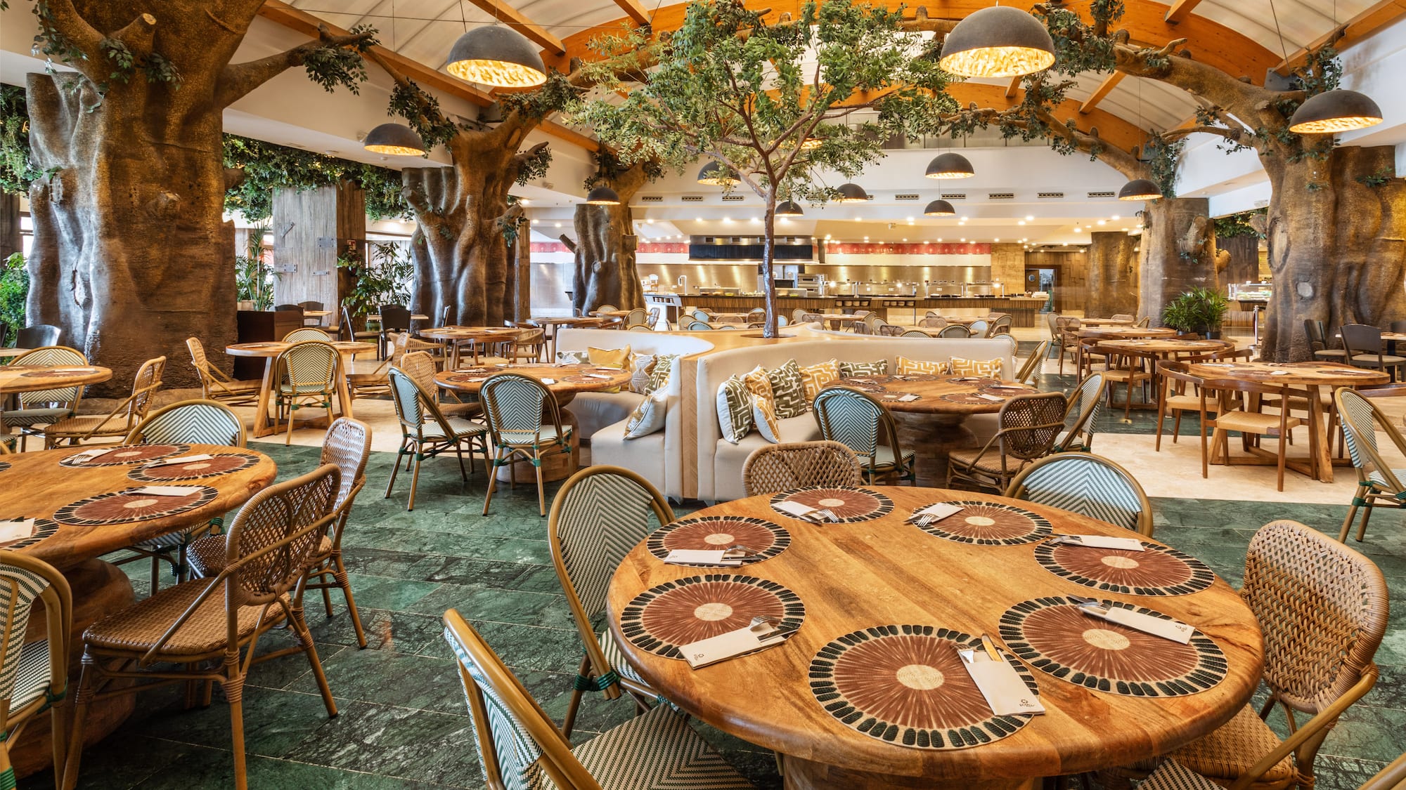 Nature-themed hotel restaurant with large trees, wooden tables, and buffet.