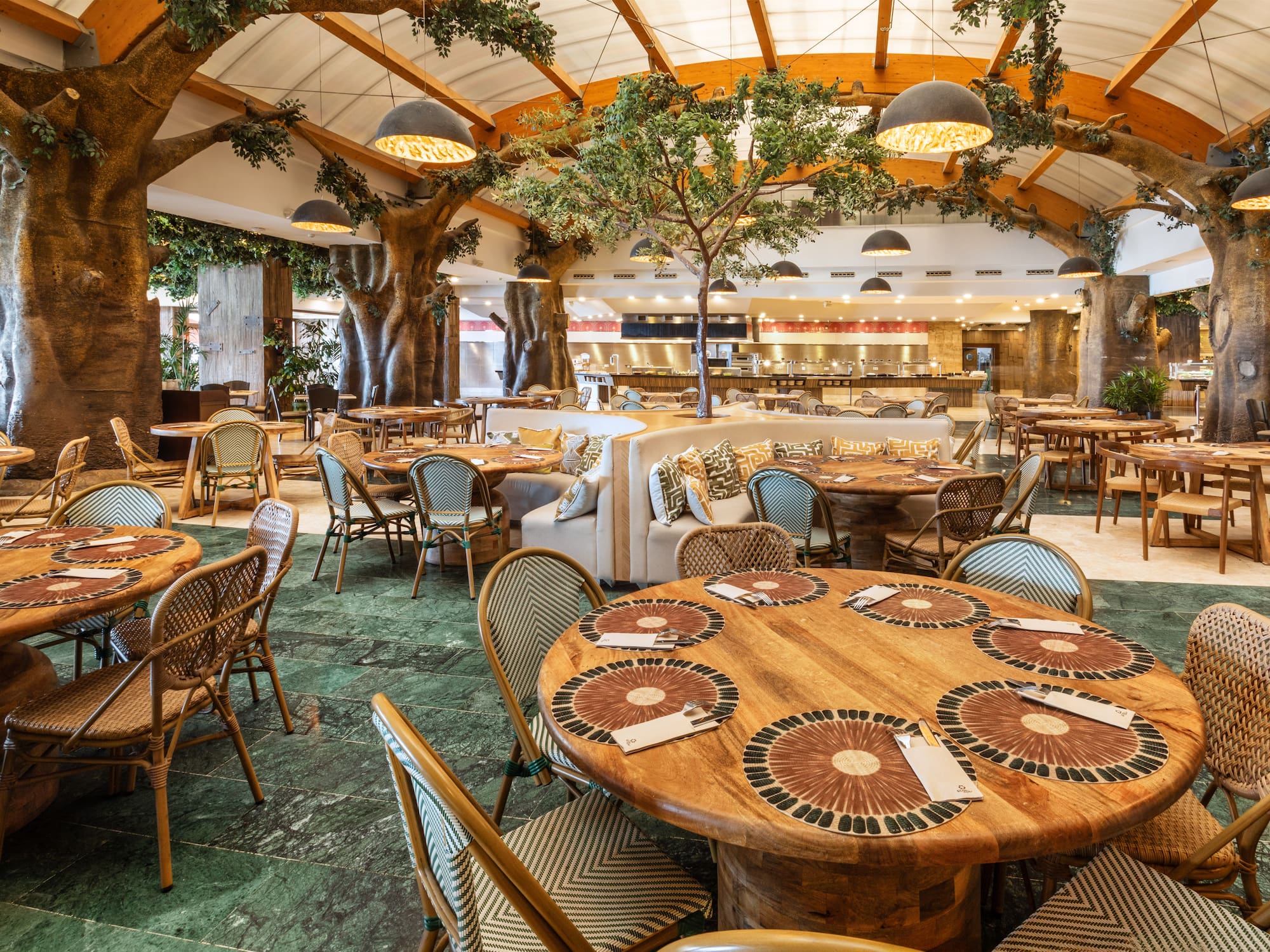 Jungle-themed restaurant with tree columns, wooden tables, green floor, and buffet.