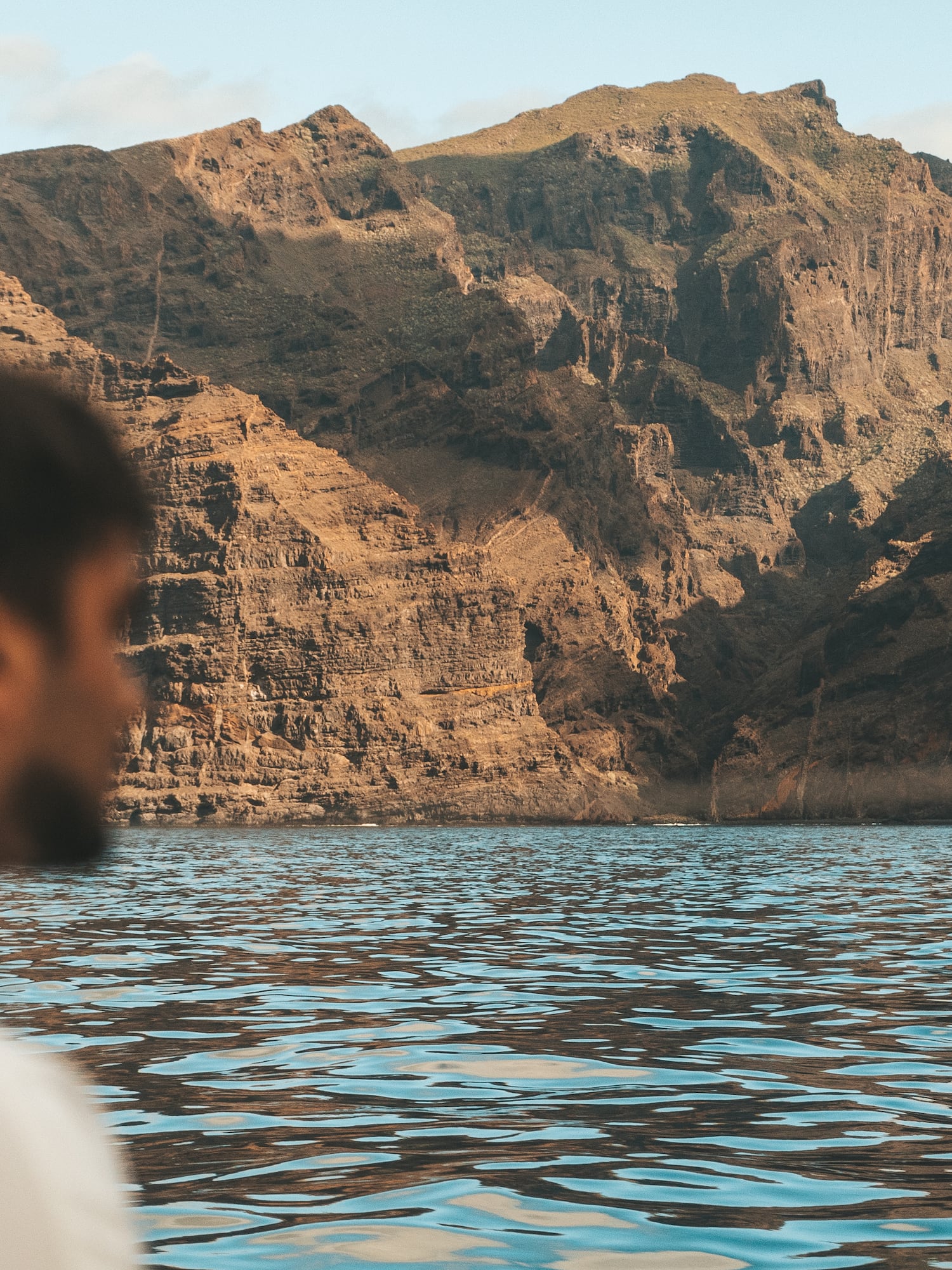 a man sitting in front of a body of water with mountains in the background