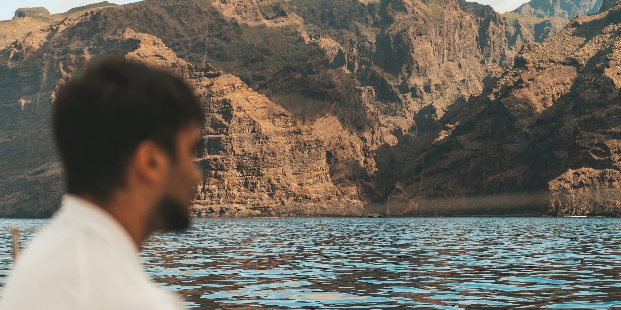 a man sitting in front of a body of water with mountains in the background