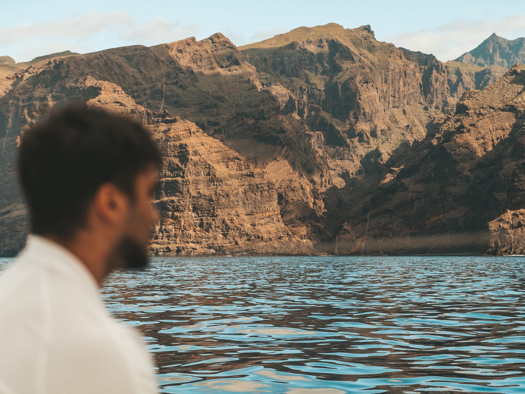 a man sitting in front of a body of water with mountains in the background