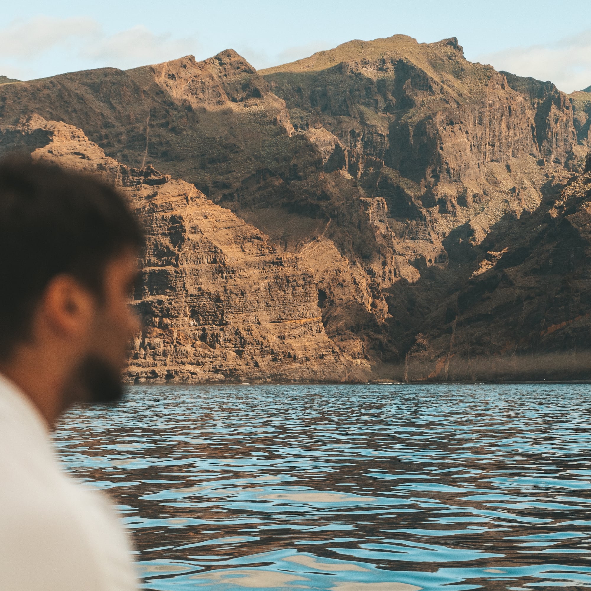 a man sitting in front of a body of water with mountains in the background