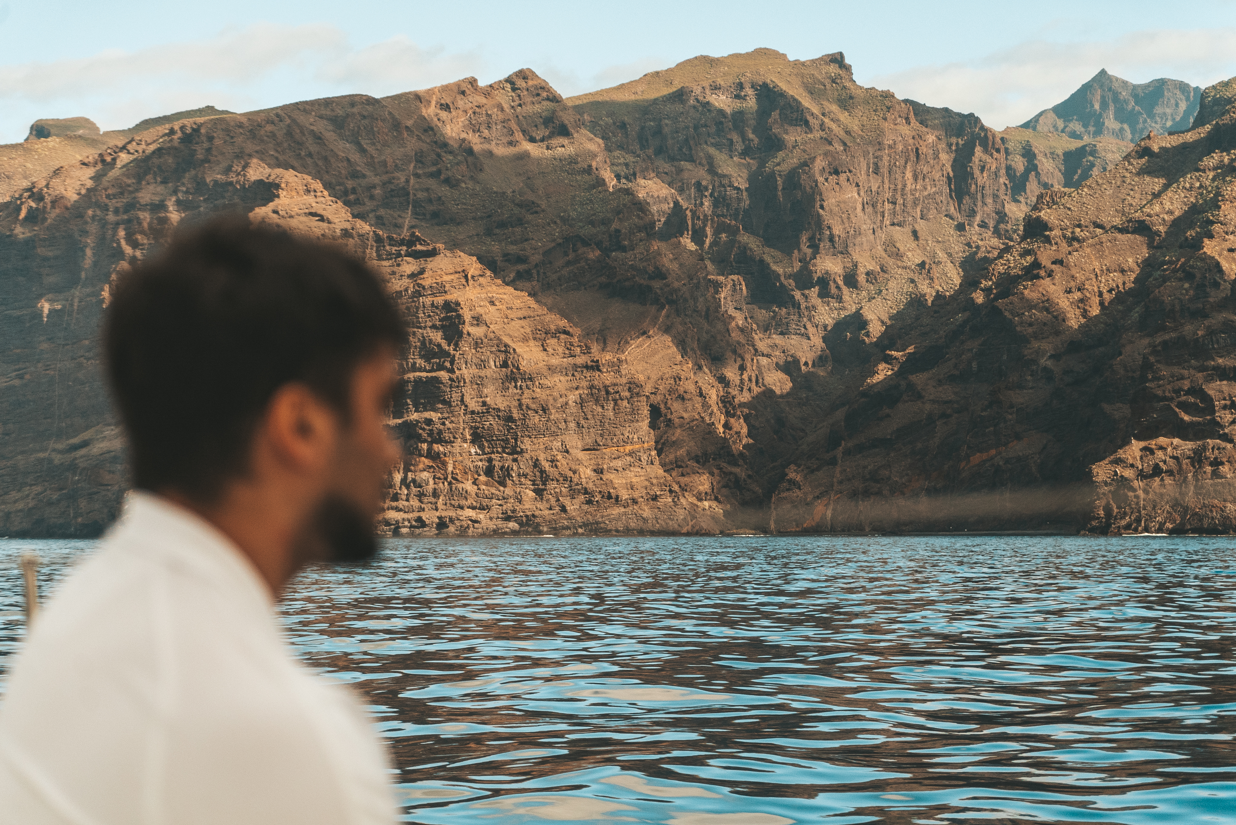 a man sitting in front of a body of water with mountains in the background