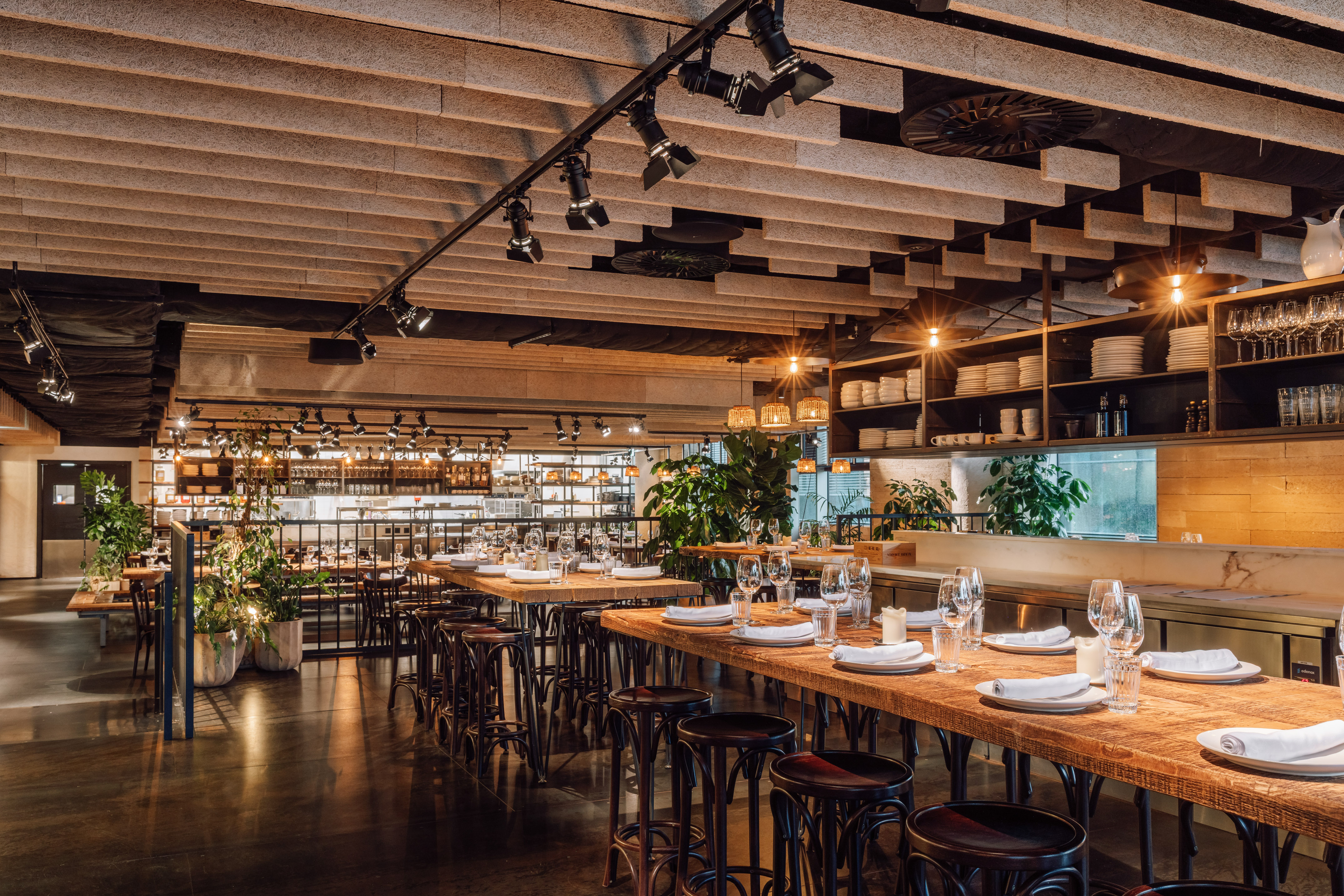 Modern restaurant dining area with wooden tables, bar seating, open kitchen.