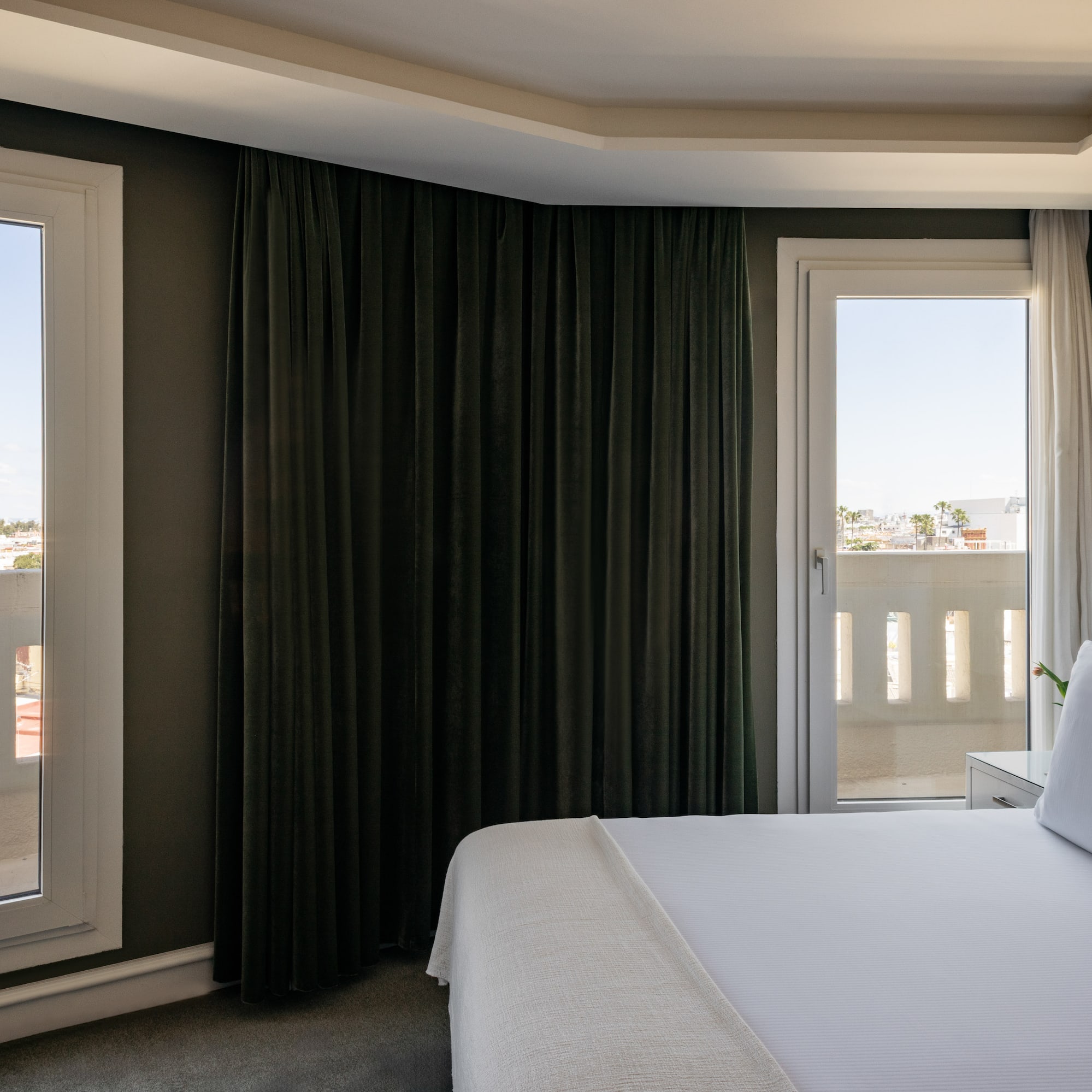 a bed with white sheets and a black curtain in a room with a balcony