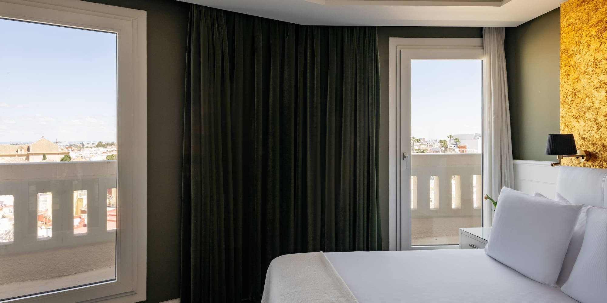 a bed with white sheets and a black curtain in a room with a balcony