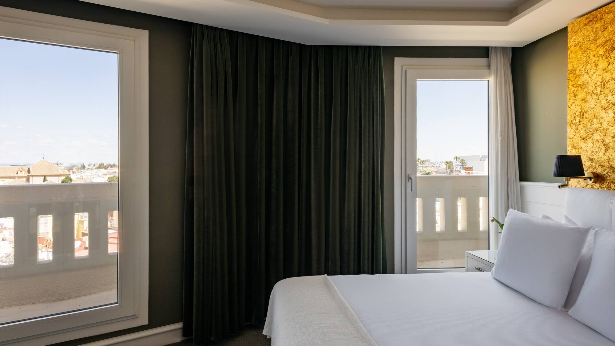 a bed with white sheets and a black curtain in a room with a balcony
