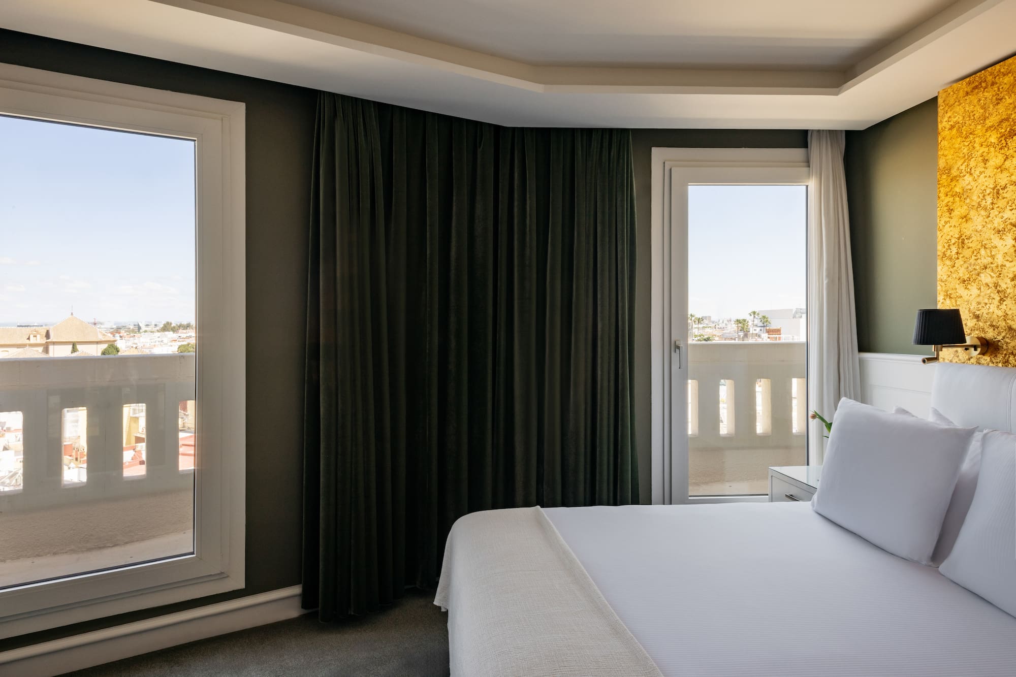 a bed with white sheets and a black curtain in a room with a balcony