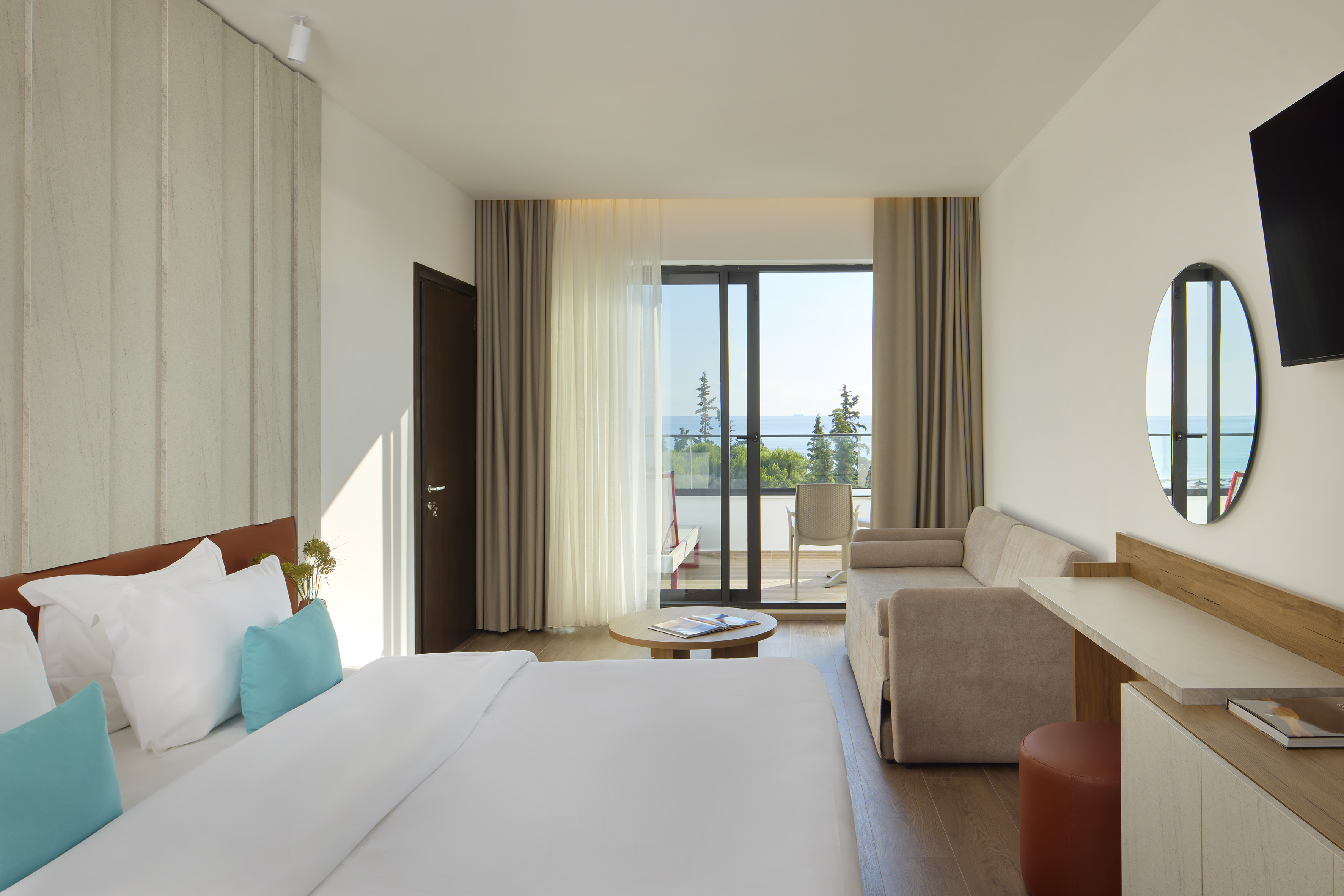 Modern hotel room with sea view balcony, large bed, and sofa.