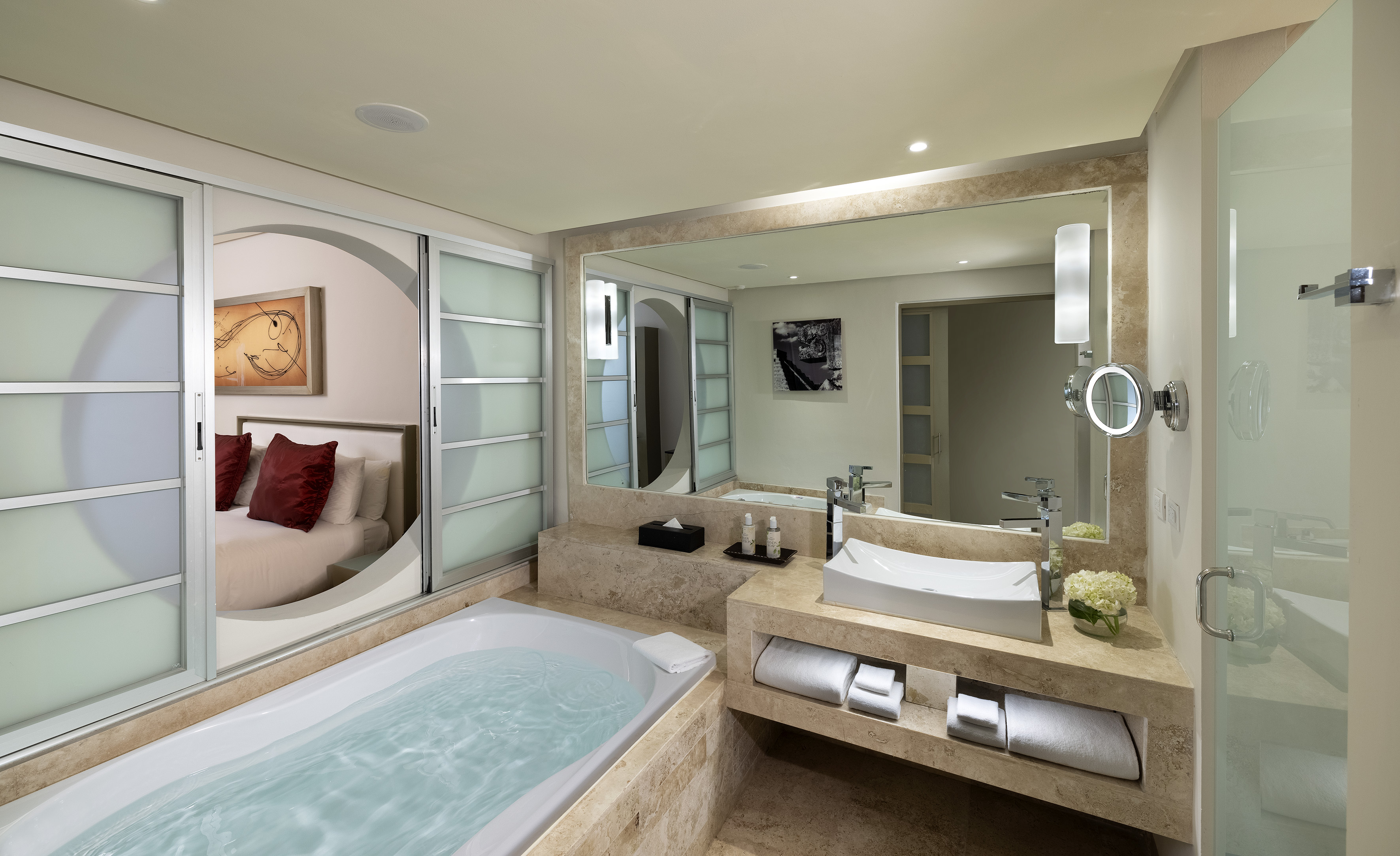 Modern hotel bathroom with bathtub, vessel sink, and sliding bedroom doors.