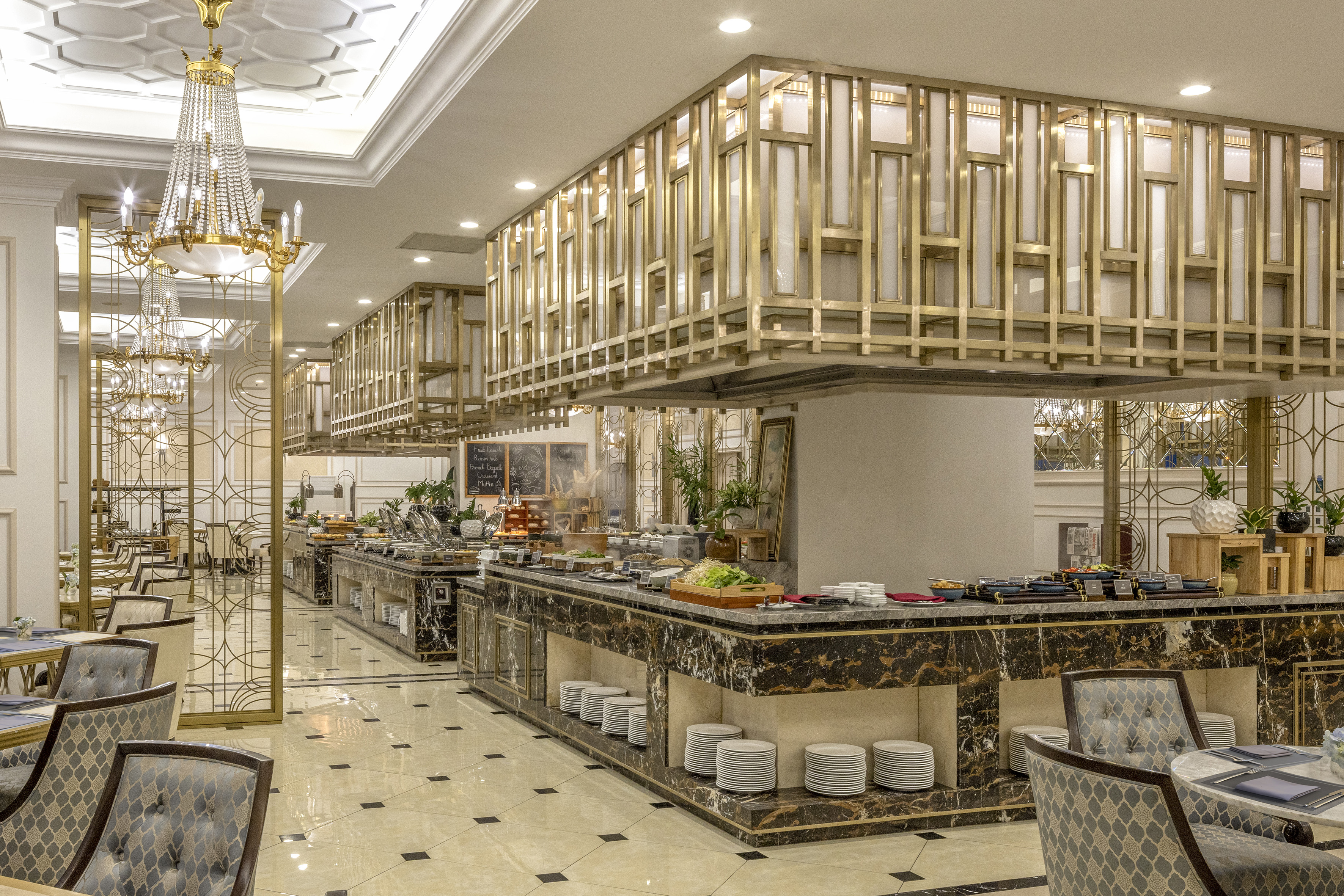 Elegant hotel buffet dining with marble counters, gold decor, and chandeliers.