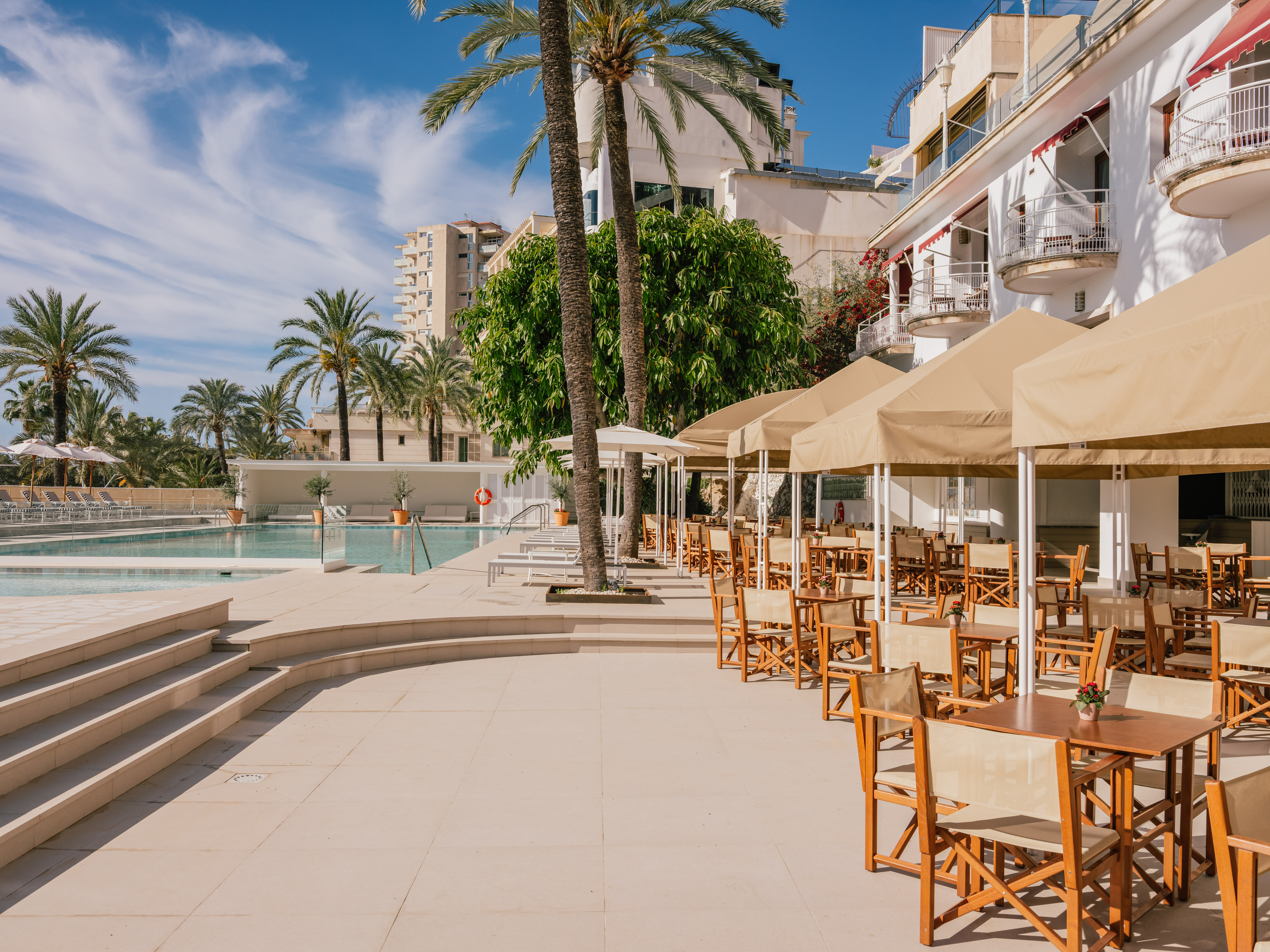 Sunny resort pool and outdoor dining patio with palm trees.