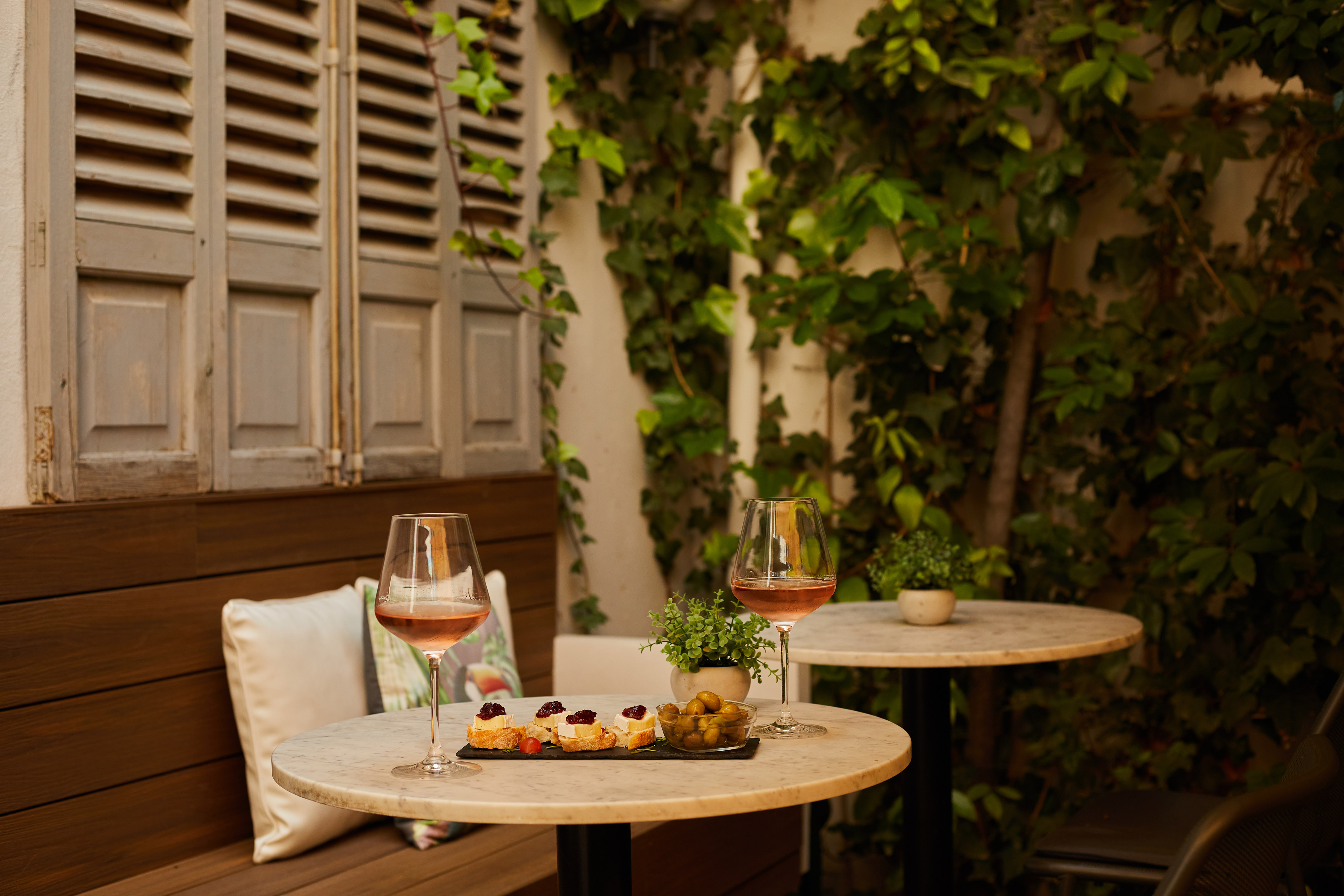 Rosé wine and appetizers on an outdoor patio table with green ivy backdrop.