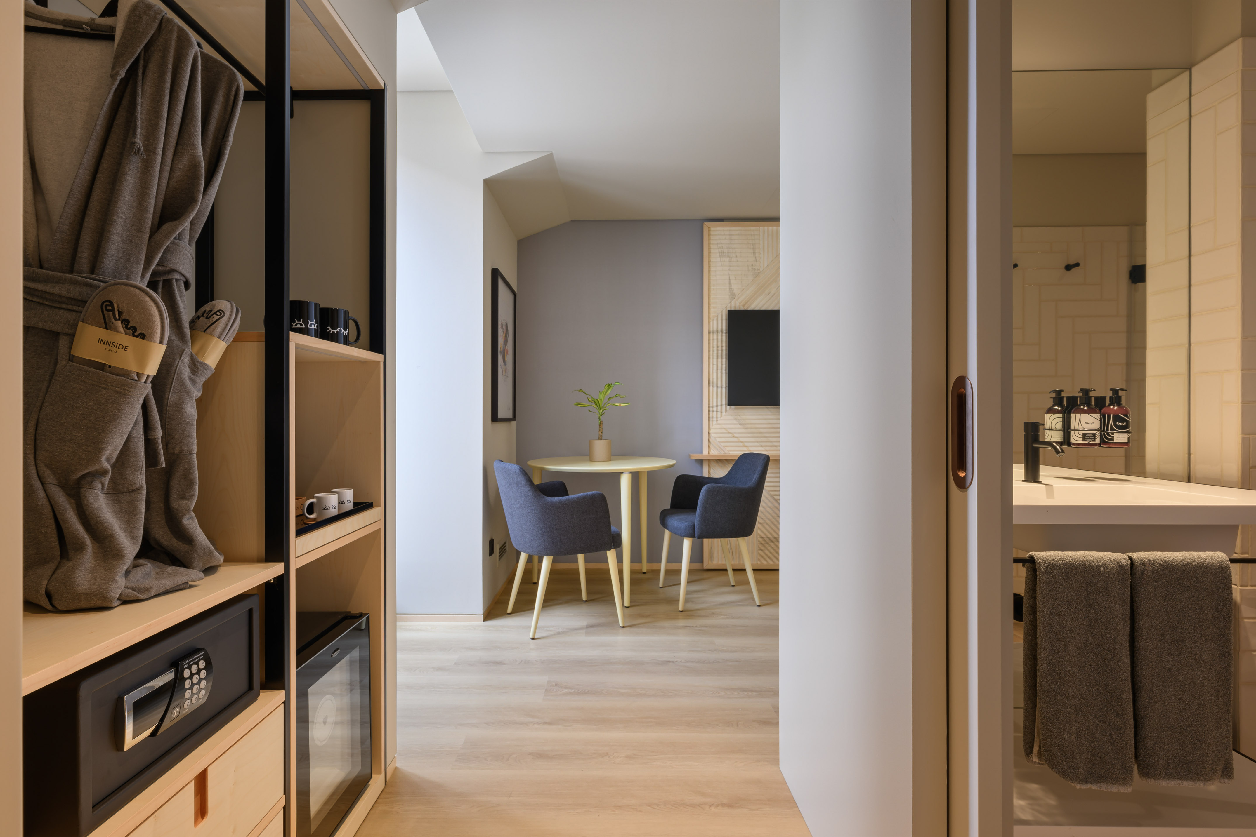 Modern hotel room interior with open wardrobe, dining area, and bathroom entrance.