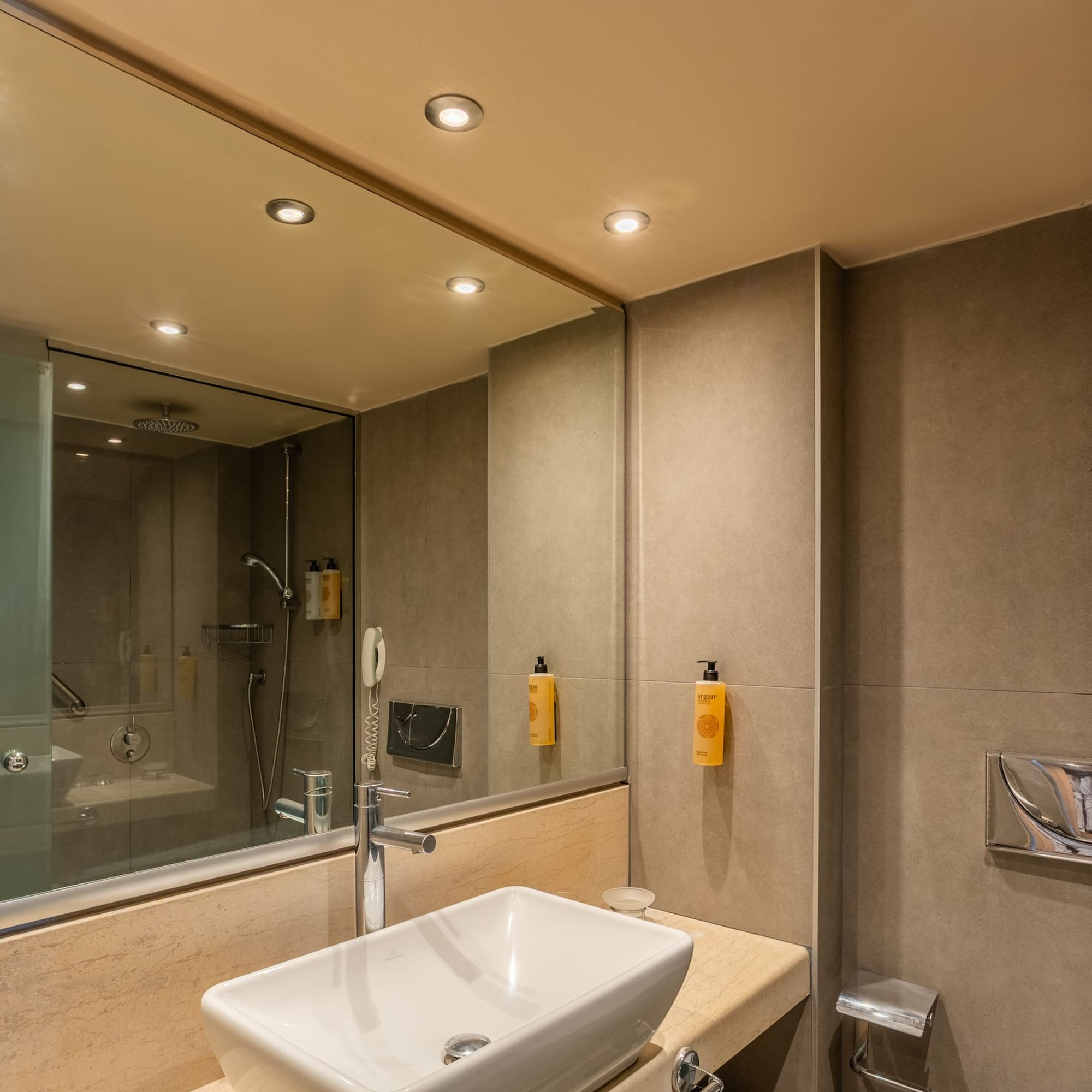 Modern hotel bathroom vanity with sink, marble counter, shower, and toilet.