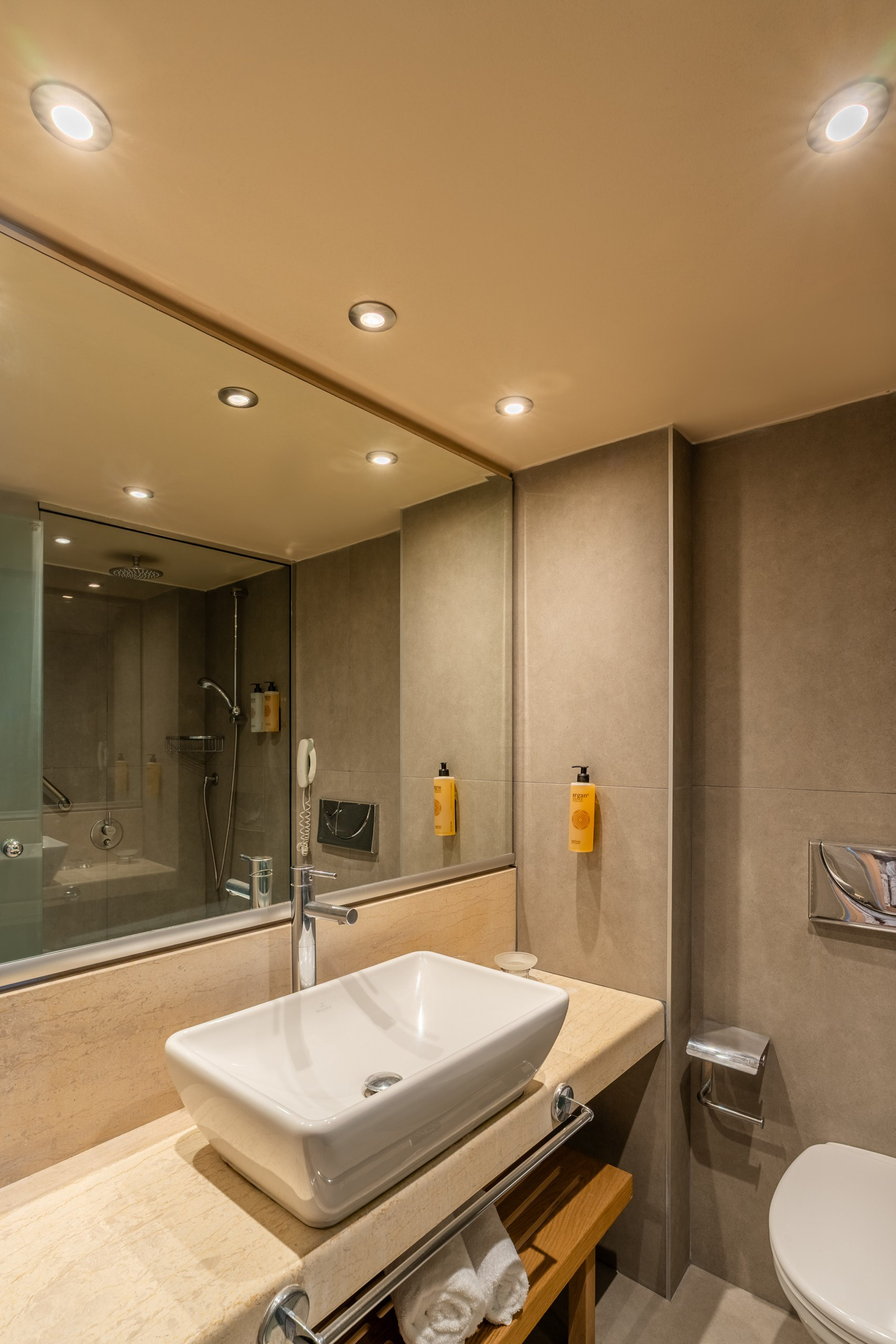 Modern hotel bathroom vanity with sink, marble counter, shower, and toilet.