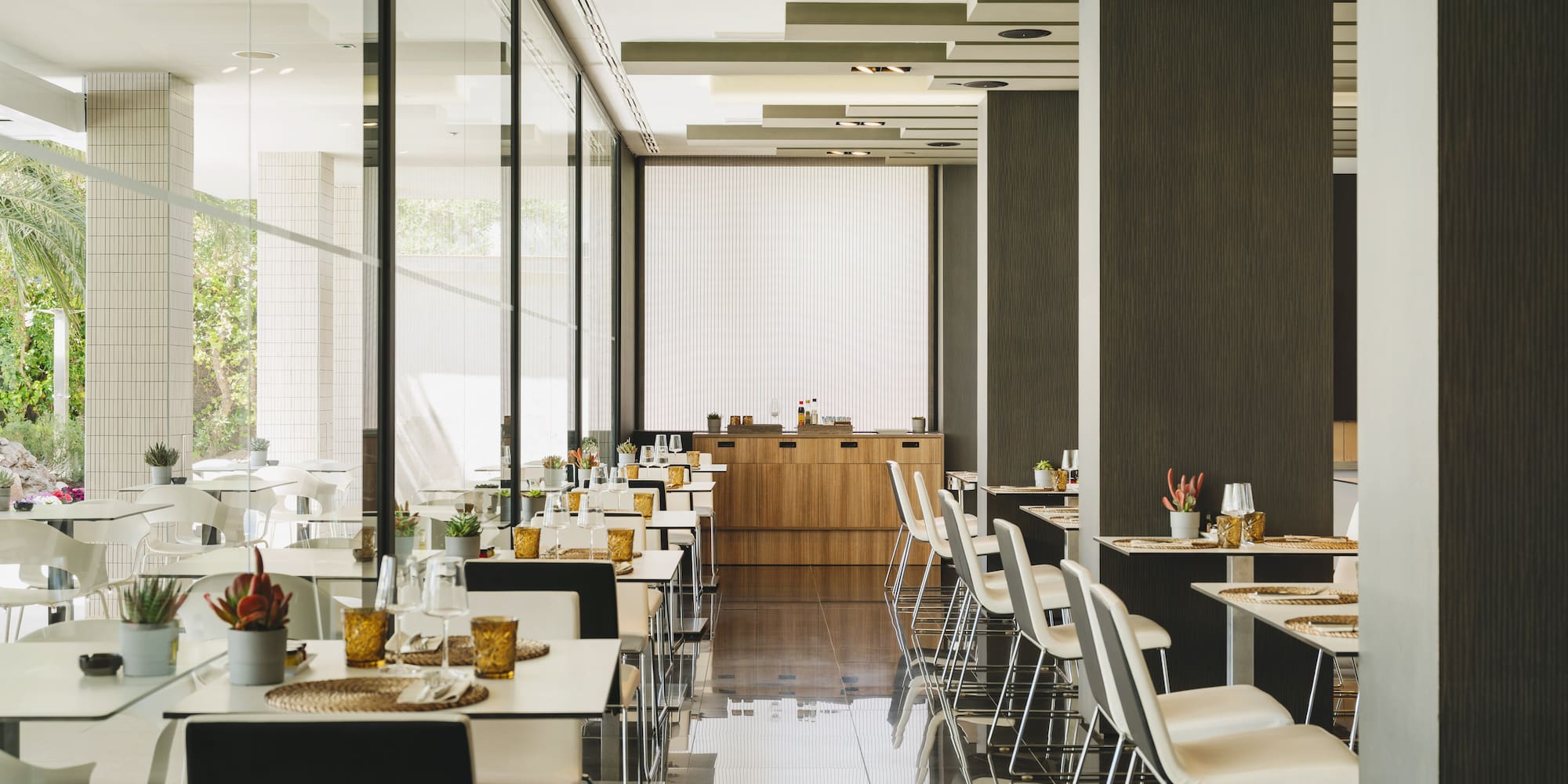 Restaurante moderno y luminoso con mesas puestas y grandes ventanales.