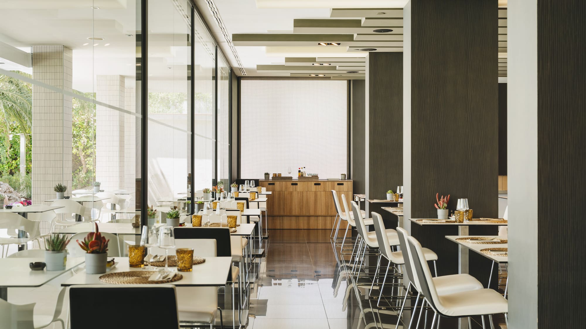 Restaurante moderno y luminoso con mesas puestas y grandes ventanales.