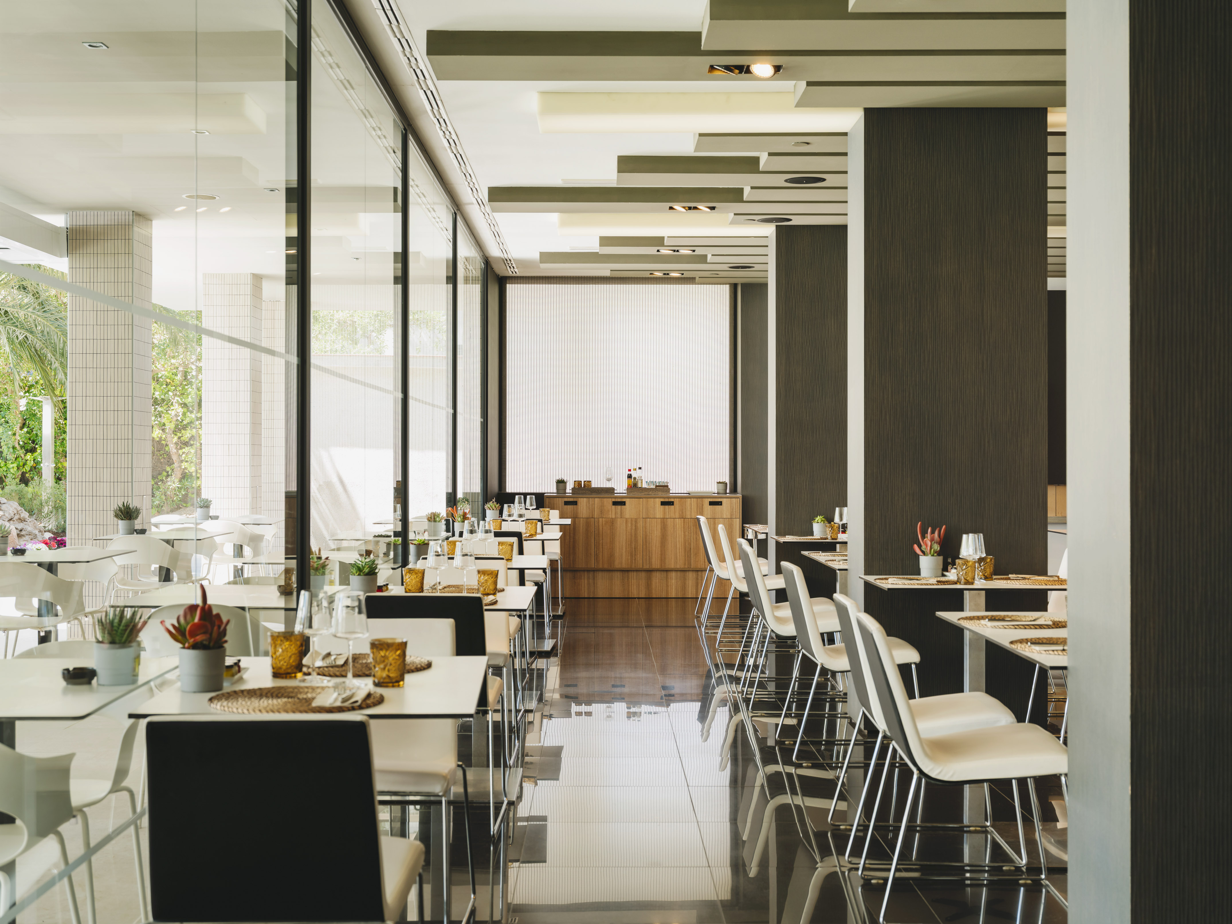 Restaurante moderno y luminoso con mesas puestas y grandes ventanales.