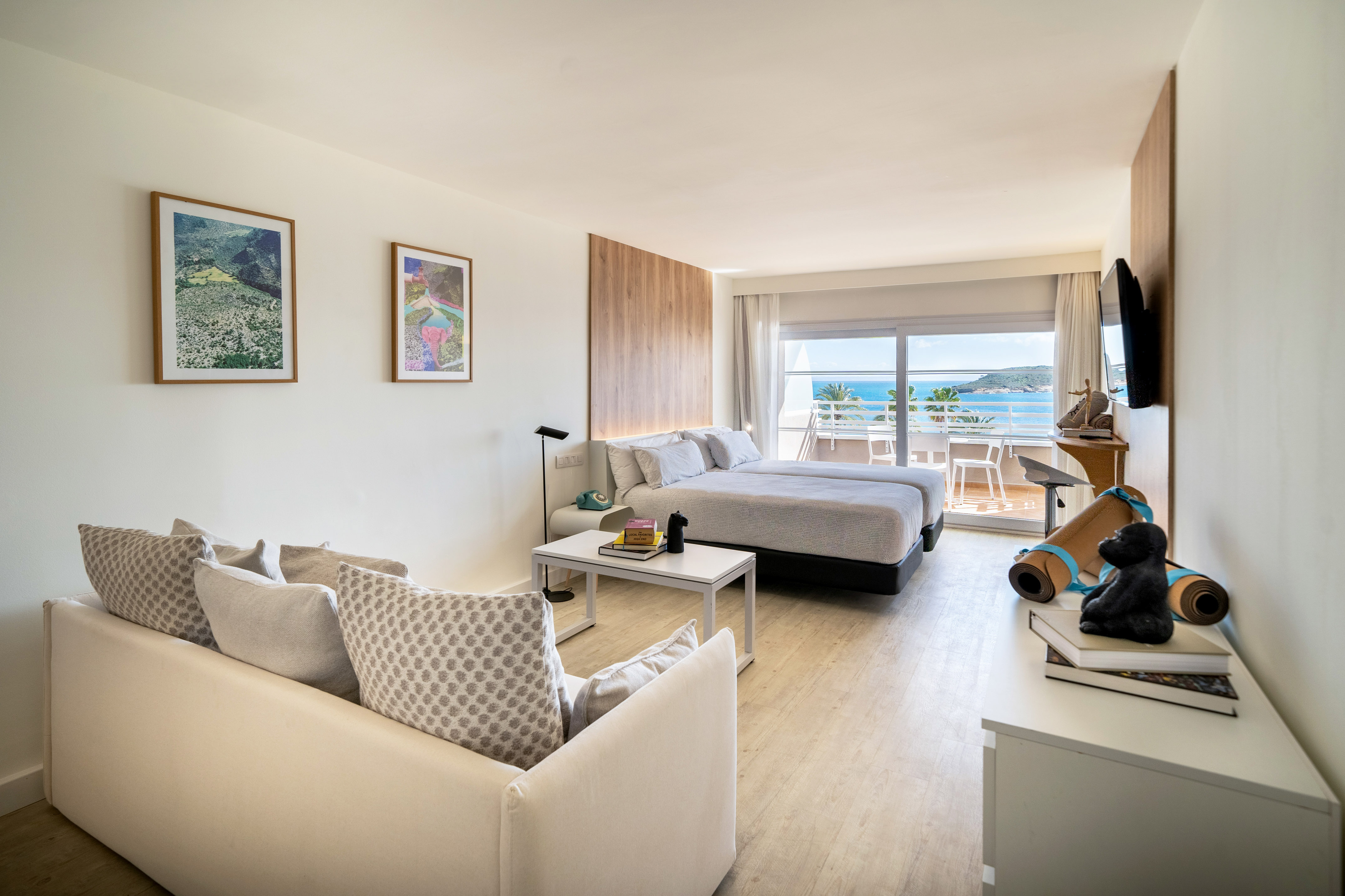 Bright hotel room with twin beds, living area, and balcony with sea views.
