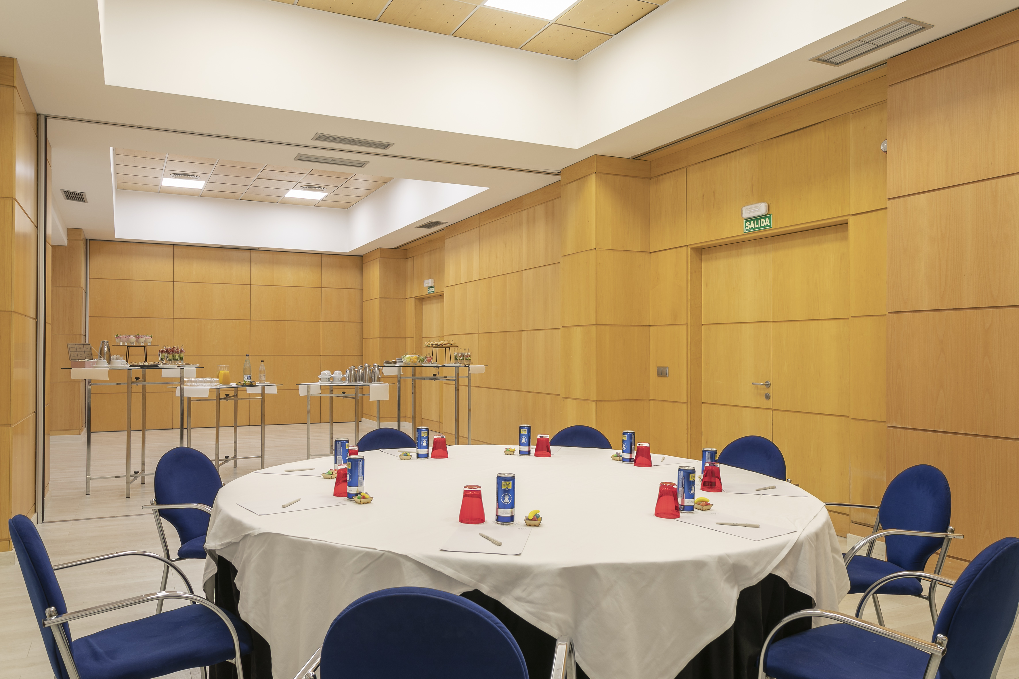 Modern conference room with round table, blue chairs, and refreshment station.