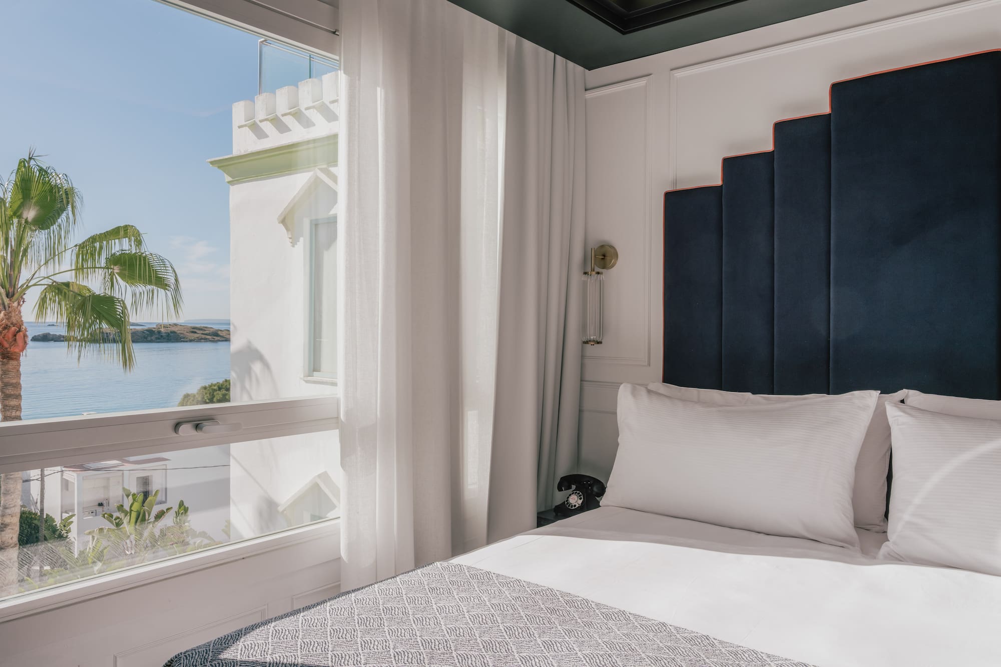 Luxury hotel room with ocean view, palm tree, and modern blue headboard.
